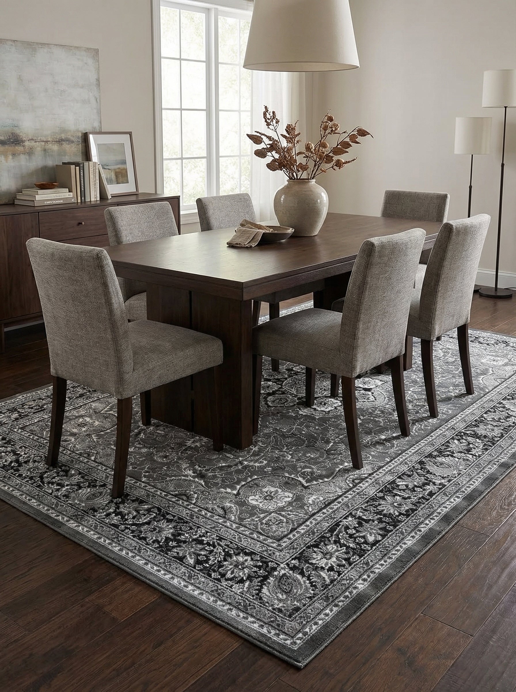 Grand tapis rectangulaire aux riches motifs floraux et arabesques dans des tons de gris, dans une salle à manger meublée