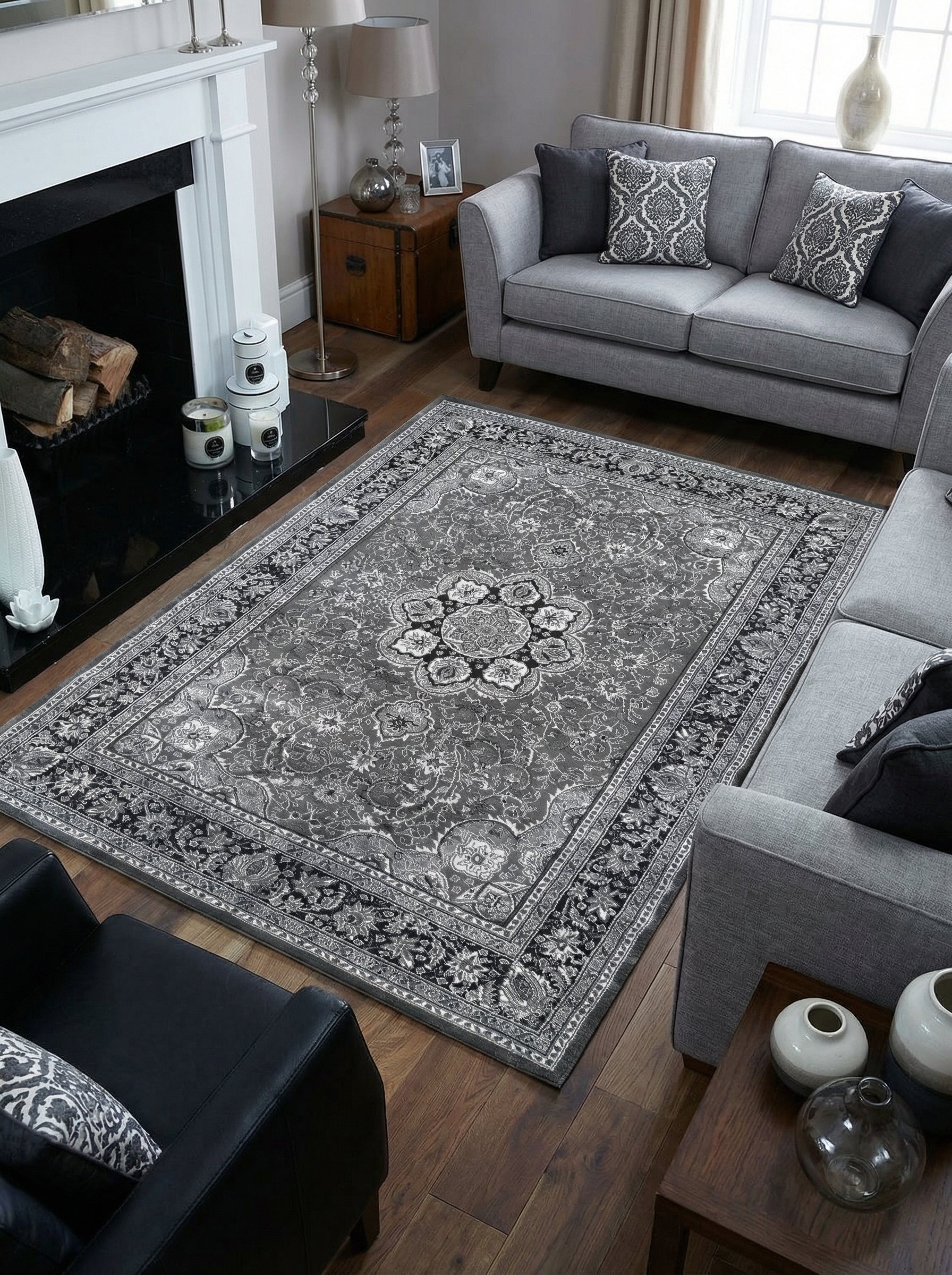 Grand tapis rectangulaire gris à motifs persans noirs et blancs, avec un médaillon central et une bordure travaillée, posé sur un parquet dans un salon