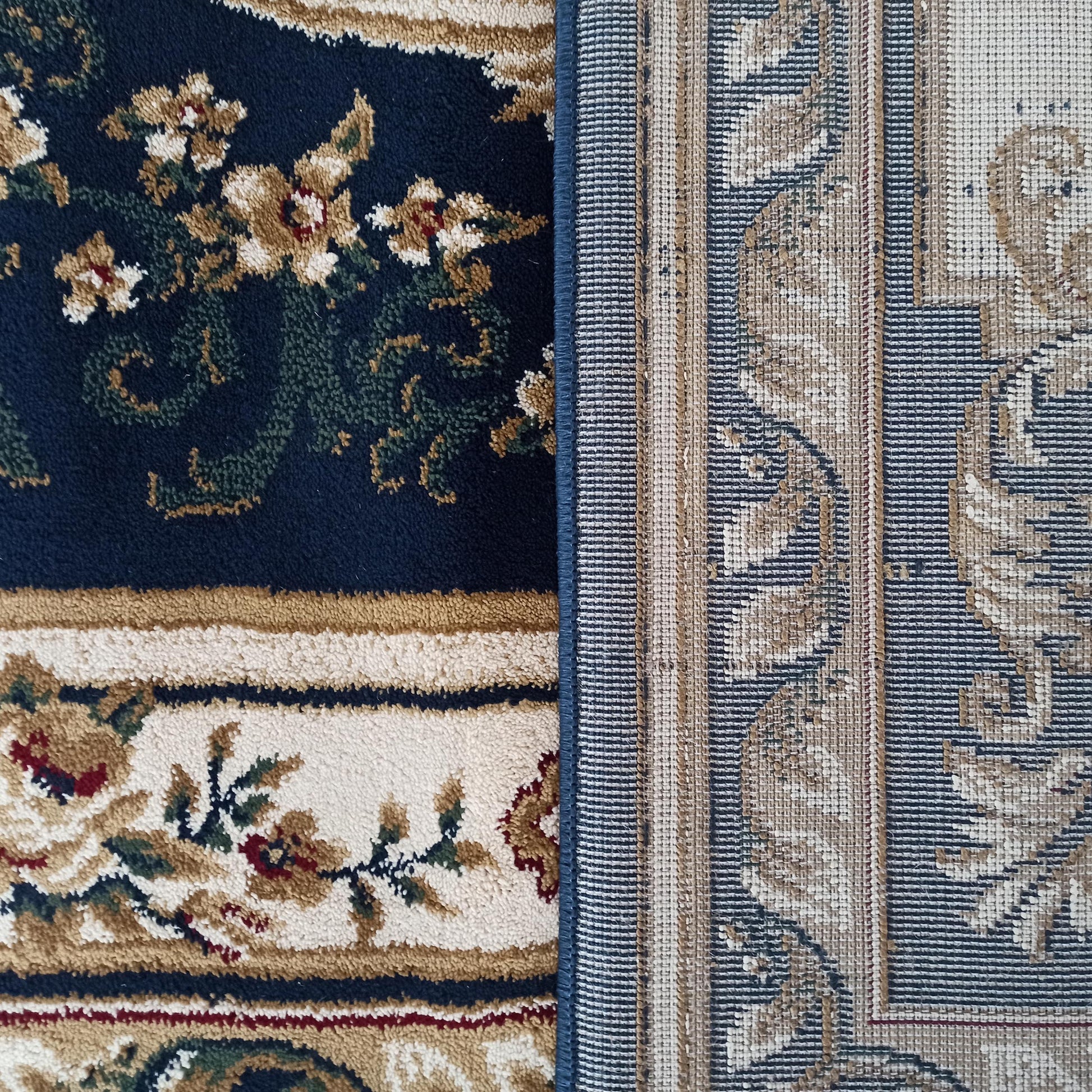 Un tapis bleu marine à motifs floraux beige, crème et rouge, et un second tapis au revers tissé à rayures beiges et bleues