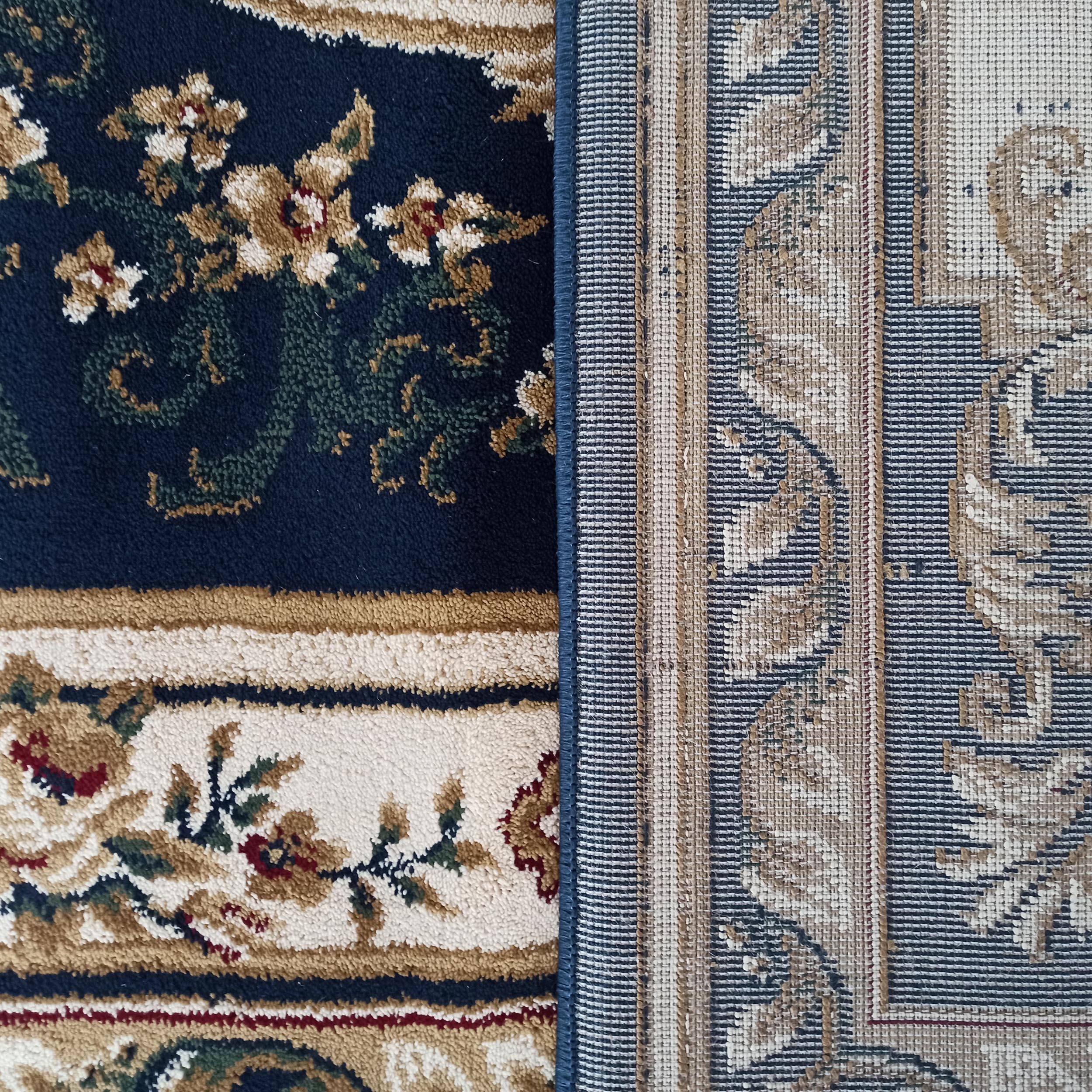 Un tapis bleu marine à motifs floraux beige, crème et rouge, et un second tapis au revers tissé à rayures beiges et bleues