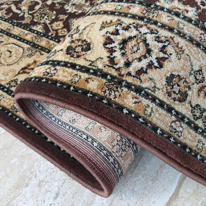 Tapis textile traditionnel partiellement roulé, aux motifs floraux beiges, marron et vert foncé, avec des bordures distinctes