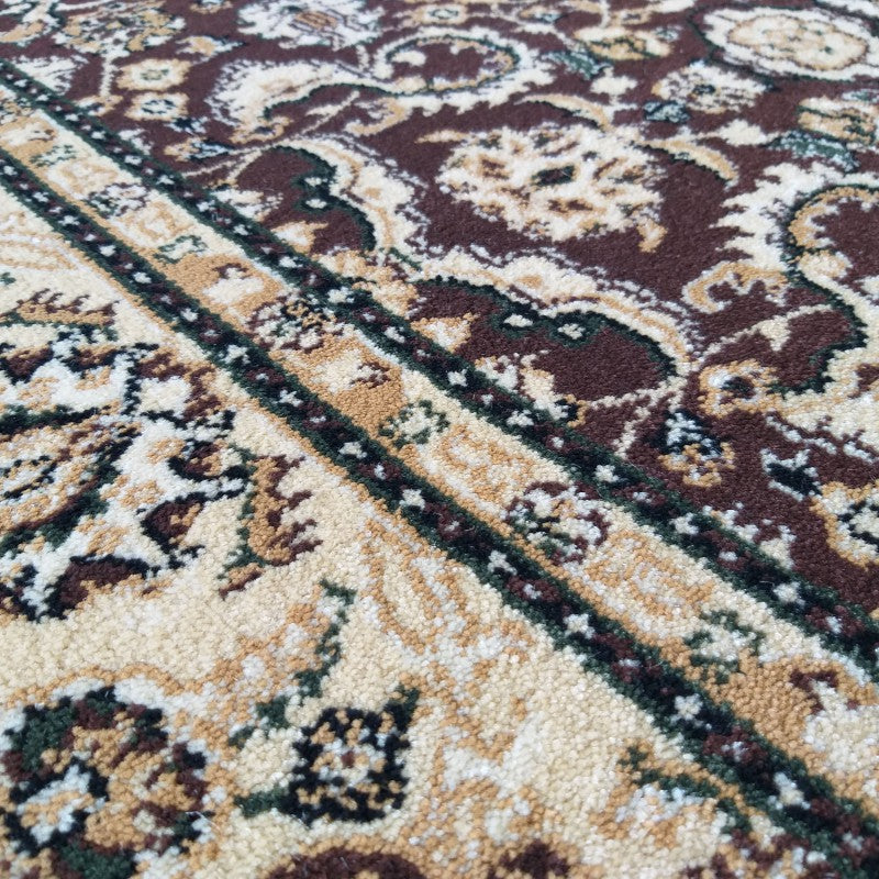 Gros plan d'un tapis aux motifs ornementaux beige crème et marron foncé, avec des touches de vert