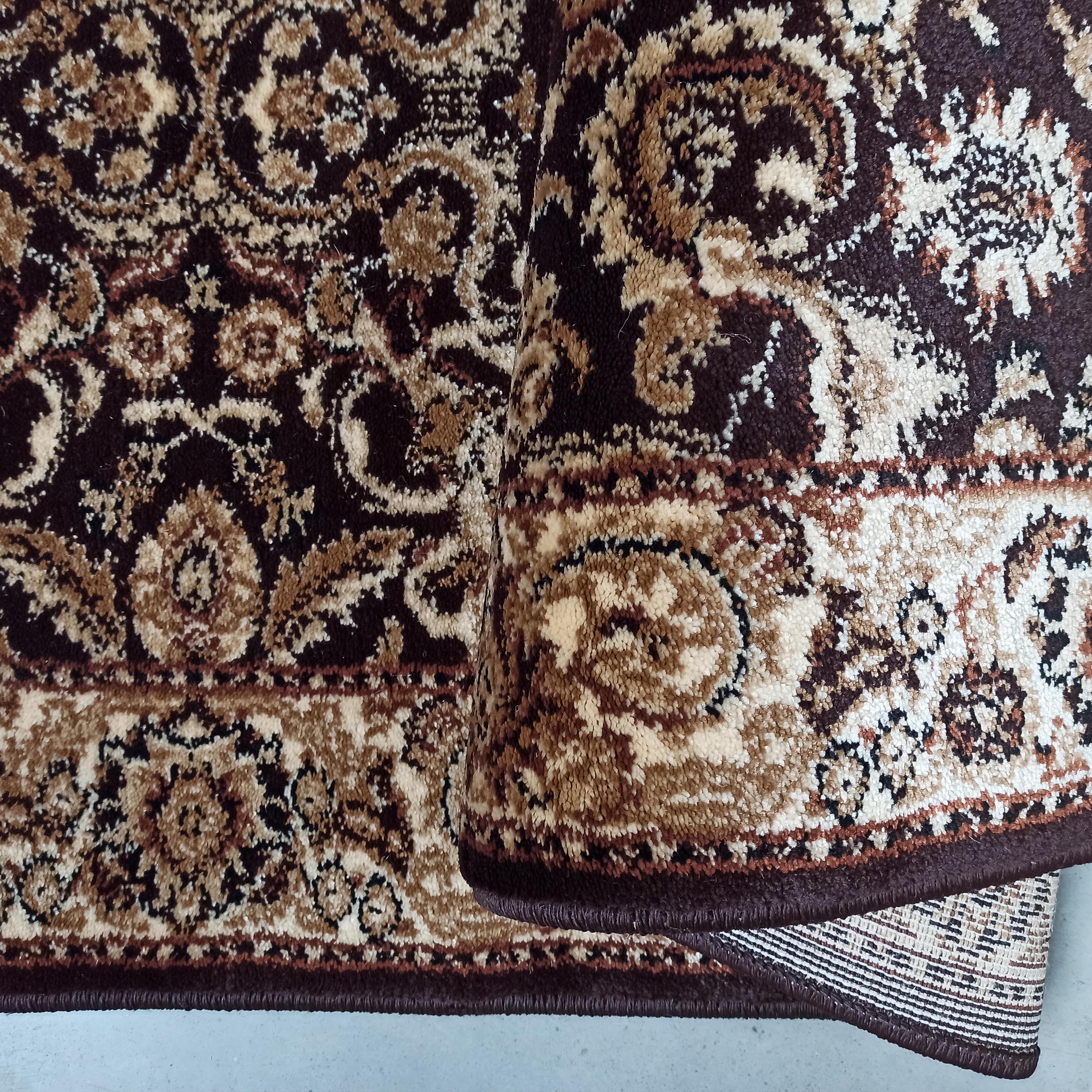 Un tapis marron foncé et beige à motifs floraux, sa surface en textile doux et son envers apparent