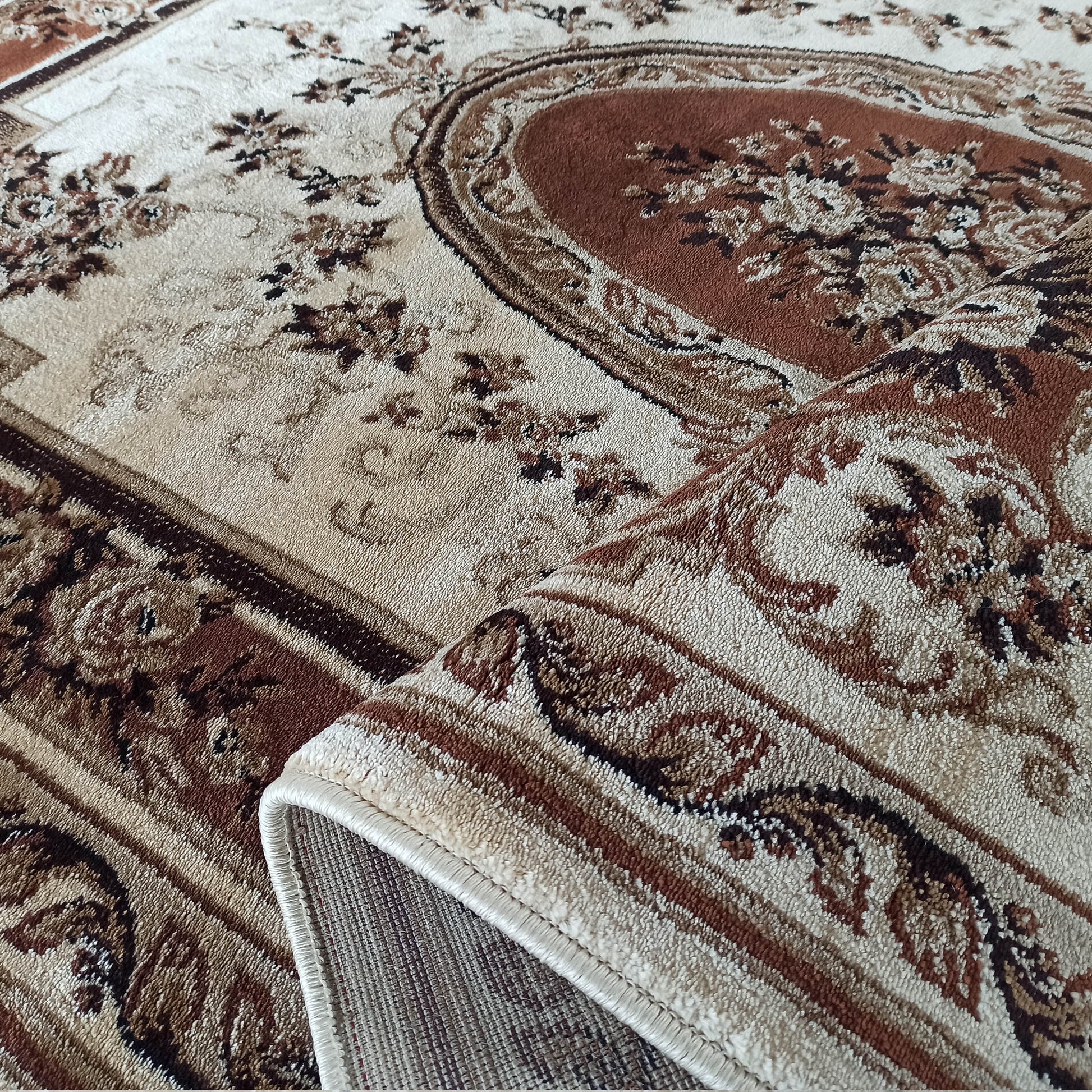 Un tapis beige et marron aux motifs floraux et ornés, montrant sa texture tissée et un coin légèrement roulé