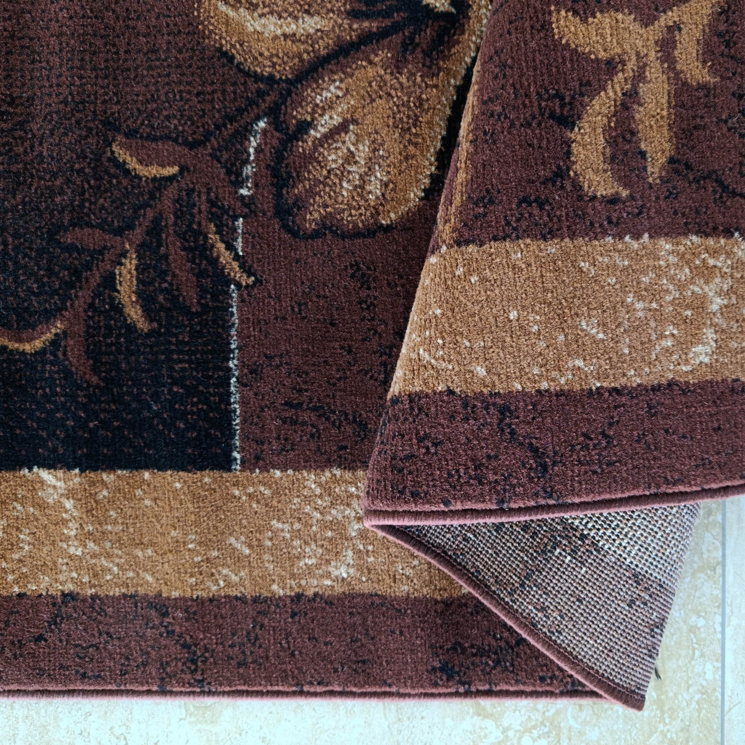 Tapis marron foncé à motifs floraux beiges et noirs, plié, montrant ses bandes et envers à carreaux sur sol carrelé clair