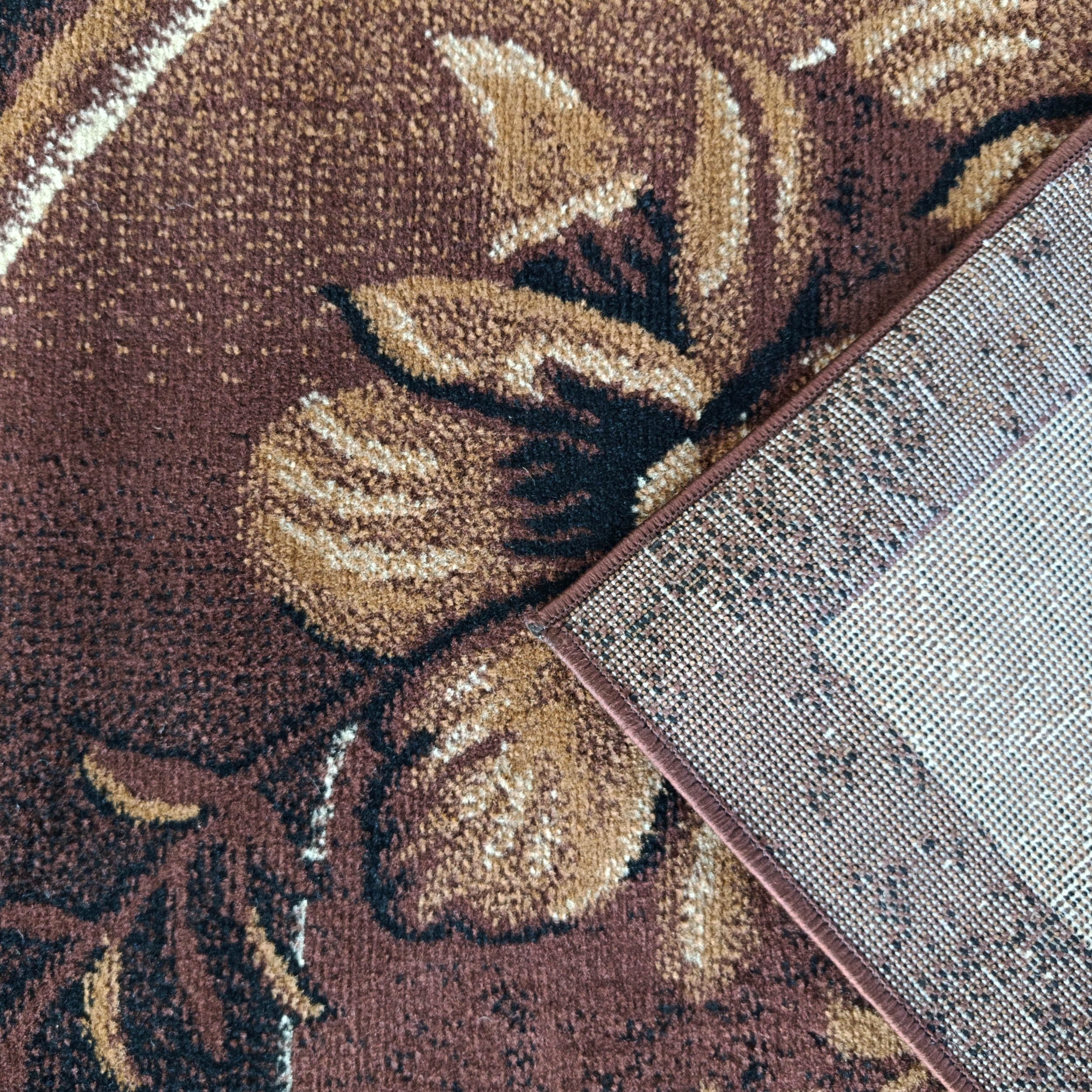 Tapis marron à motifs floraux beige, marron clair et noir, un coin est relevé montrant le dos tissé et la bordure marron