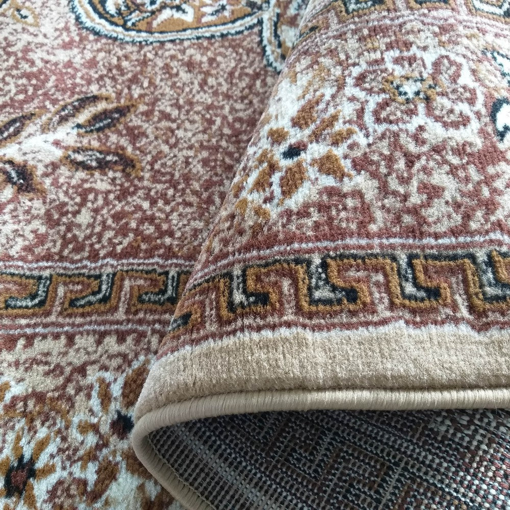 Un tapis marron et beige aux motifs floraux et géométriques complexes, légèrement roulé, montrant son envers tissé