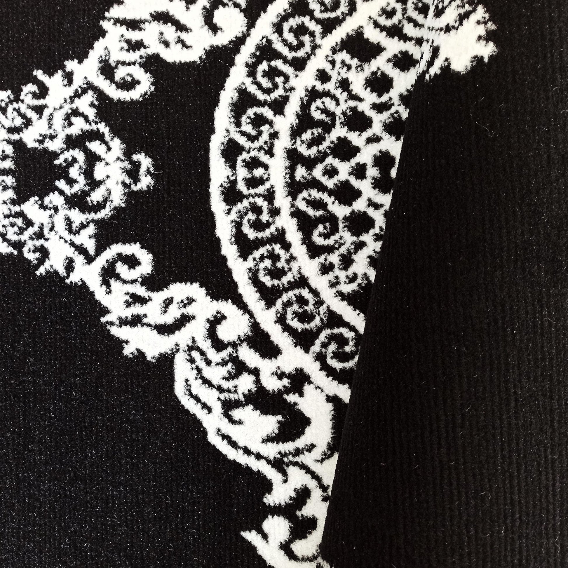 Gros plan d'un tapis textile noir et blanc, présentant un riche motif orné de volutes et d'arabesques claires sur fond sombre