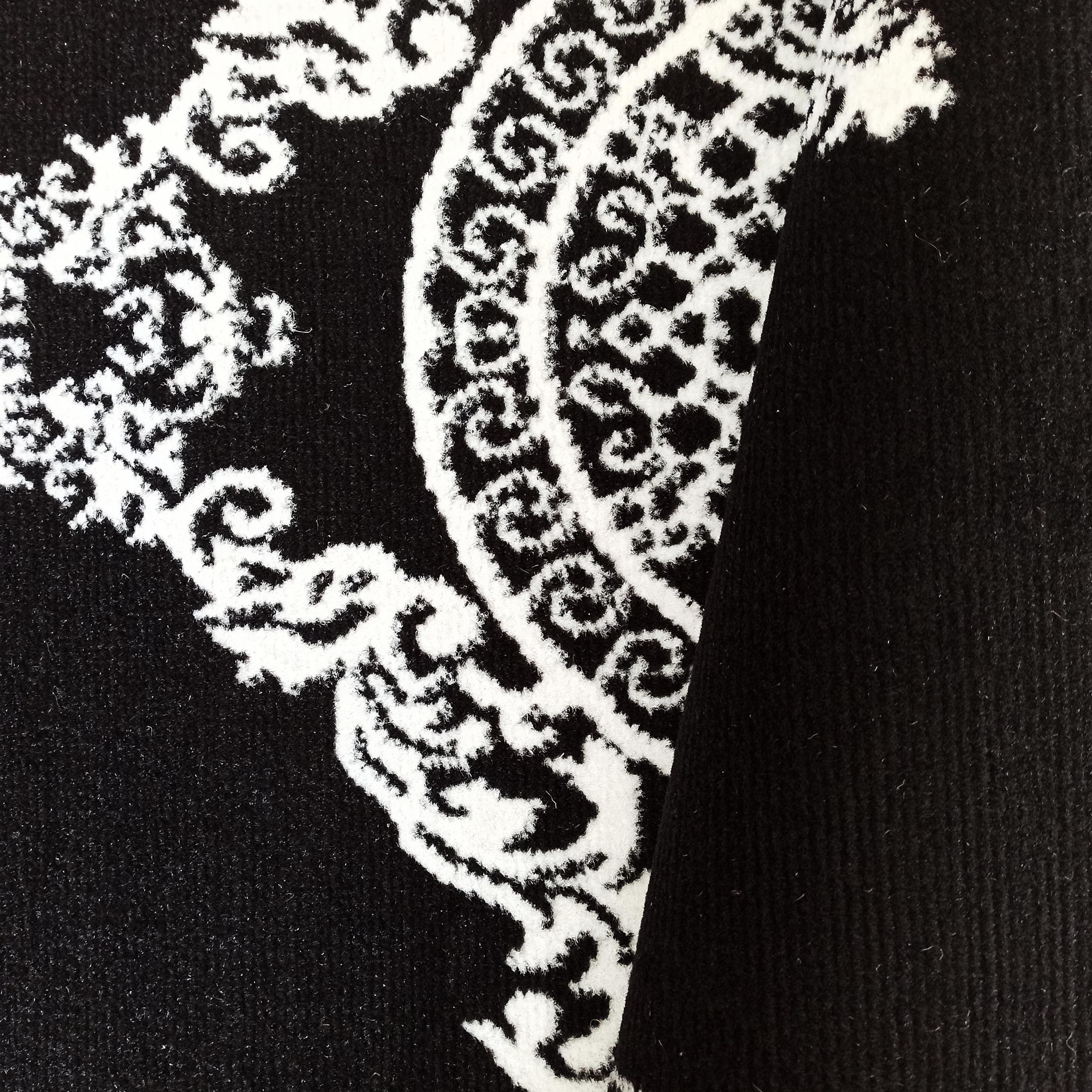 Gros plan d'un tapis textile noir et blanc, présentant un riche motif orné de volutes et d'arabesques claires sur fond sombre