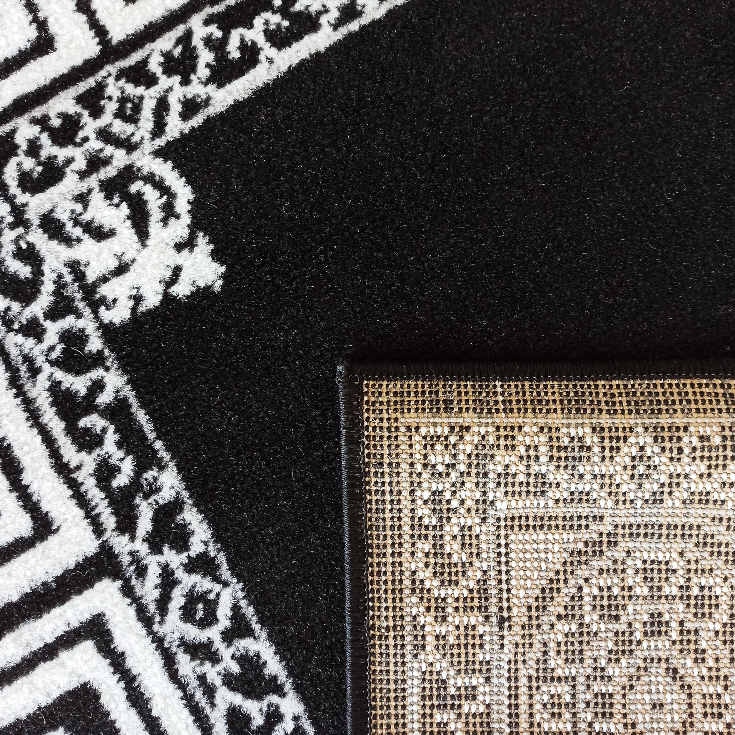 Tapis noir à motifs blancs géométriques et ornementaux, dont le revers est un tissage beige clair et noir
