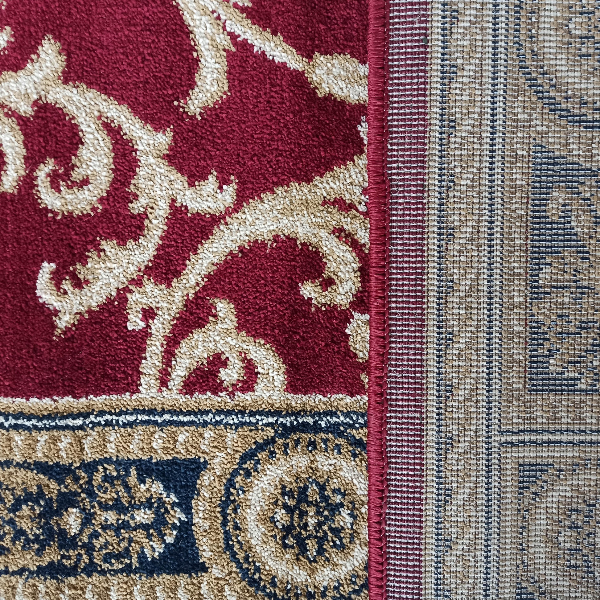 Tapis bordeaux à motifs ornementaux crème et or, avec une bordure bleue marine et le tissage du revers visible