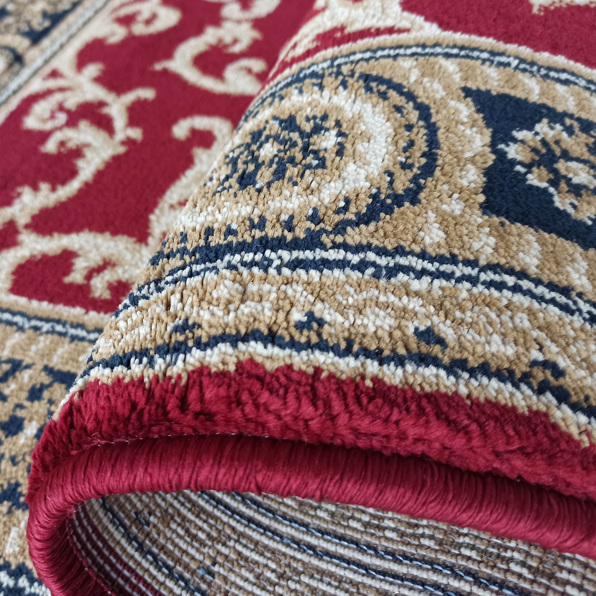Tapis doux rouge, avec des motifs ornementaux beiges, bleus et crèmes, partiellement roulé