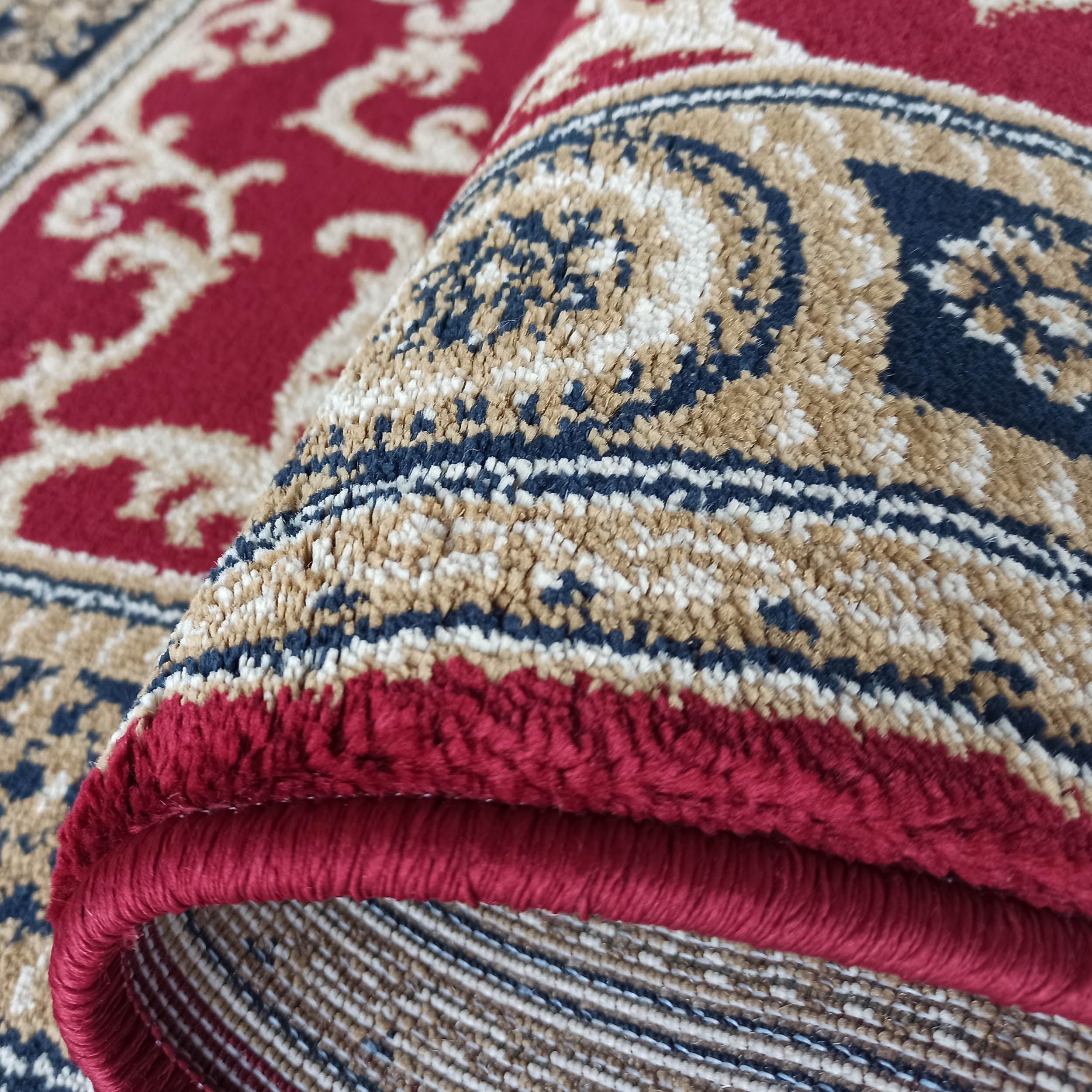 Tapis doux rouge, avec des motifs ornementaux beiges, bleus et crèmes, partiellement roulé
