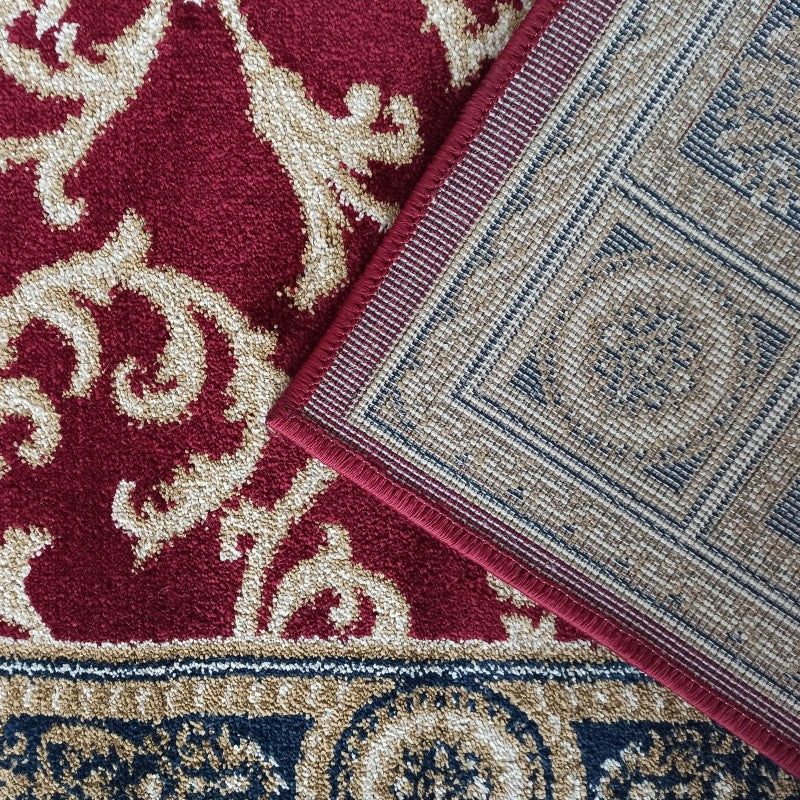 Tapis bordeaux à motifs floraux beiges et une bordure bleue, replié pour montrer son envers quadrillé beige et bleu