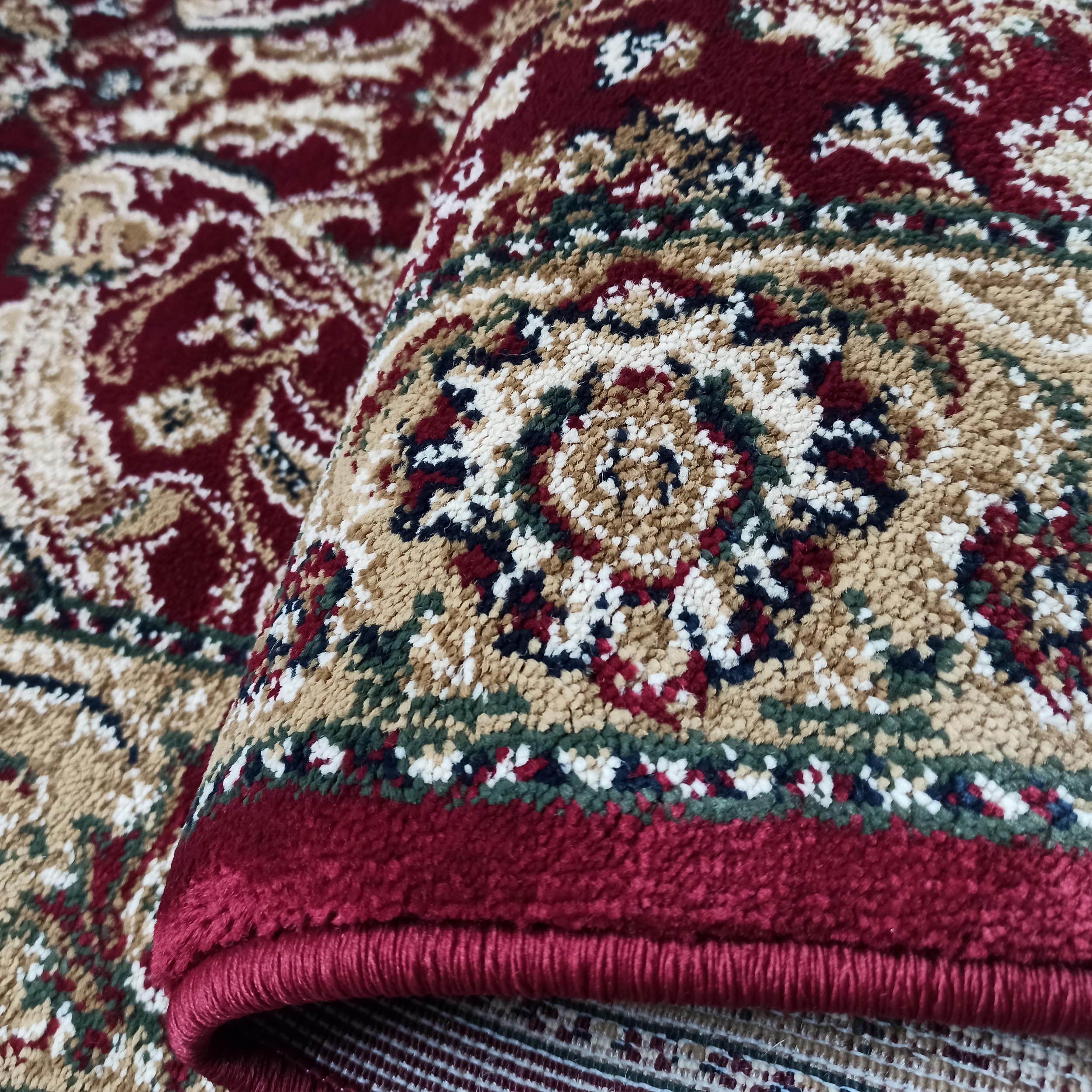 Tapis aux motifs ornementaux bordeaux, beige clair, vert forêt et crème, avec une texture dense et un bord rouge foncé apparent