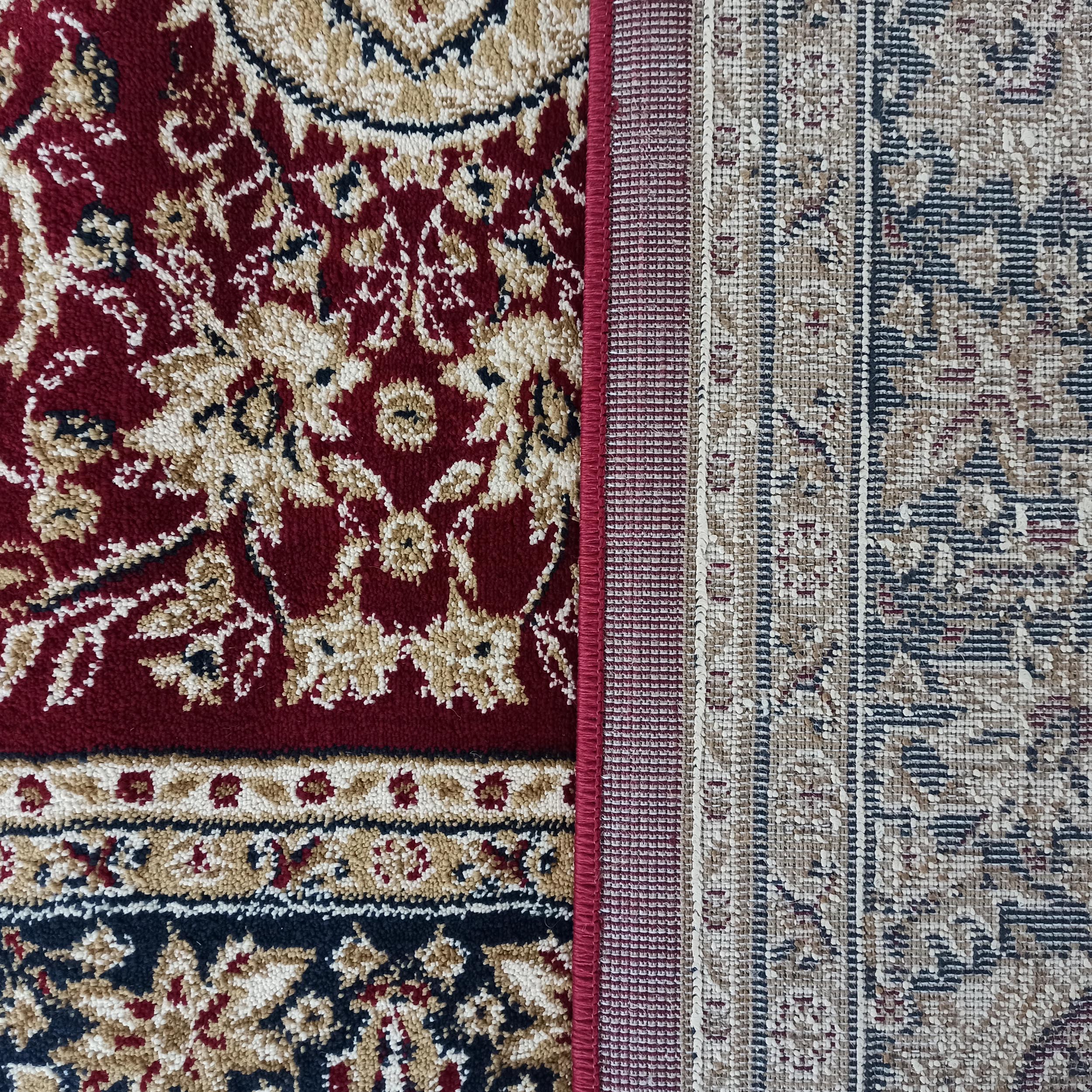 Tapis rouge à motifs floraux beiges et bleu foncé, contrastant avec un tapis tissé beige et gris à motifs géométriques