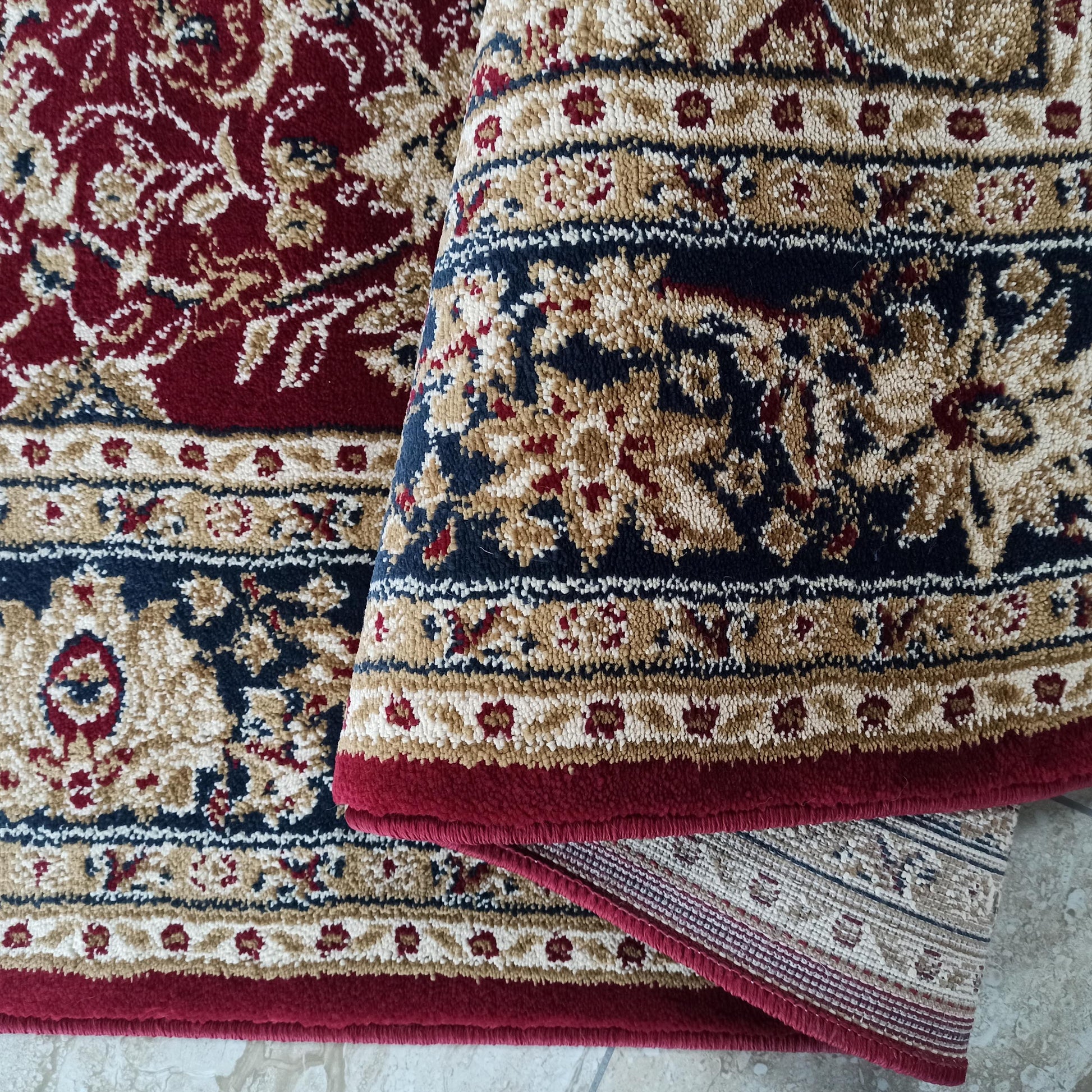 Deux sections d'un tapis à motifs floraux et arabesques. Le tapis est richement coloré en rouge bordeaux, beige et bleu foncé