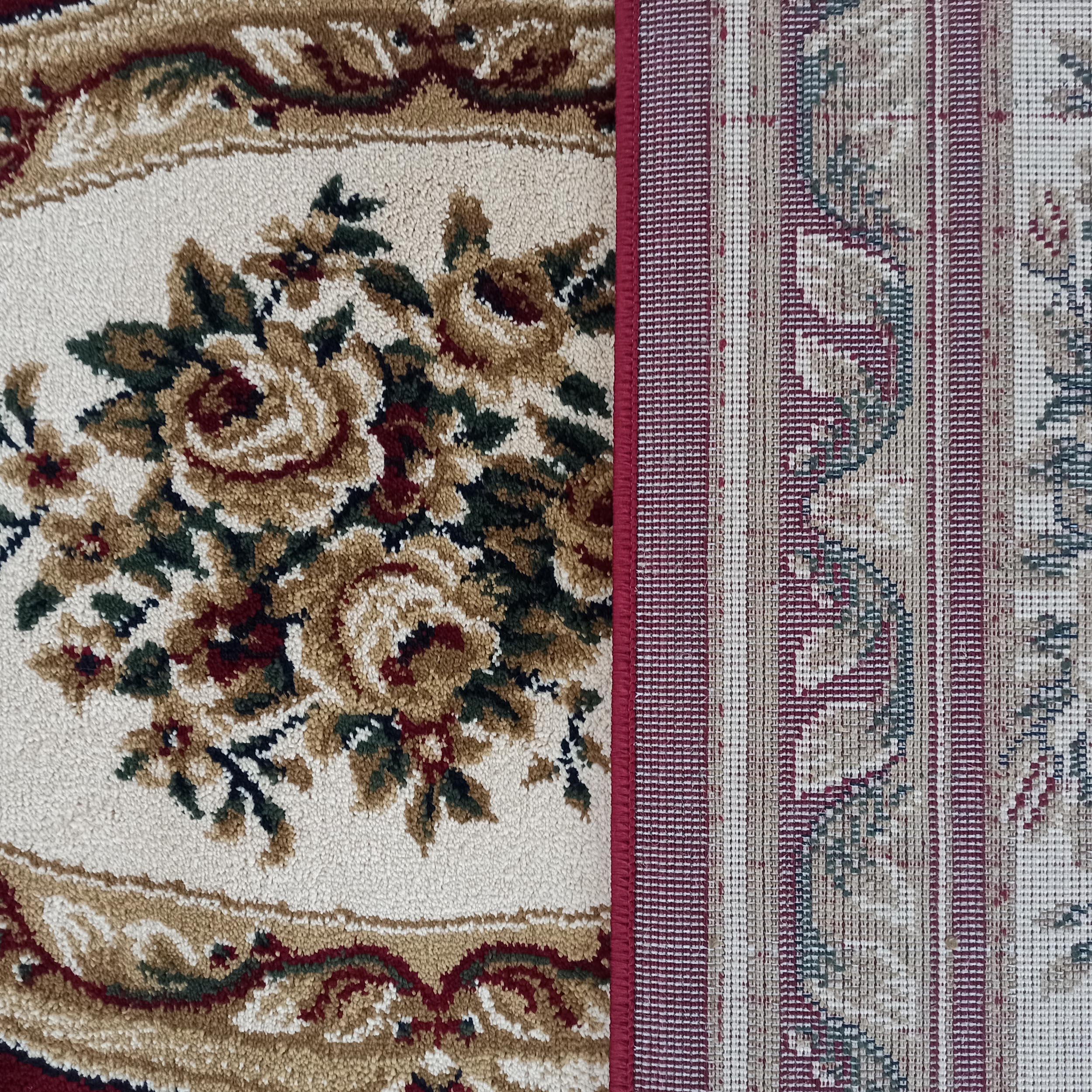 Tapis au velours floral crème, doré et rouge avec des feuilles vertes, côtoyant une section tissée à rayures rouges et beiges, séparée par un liseré bordeaux