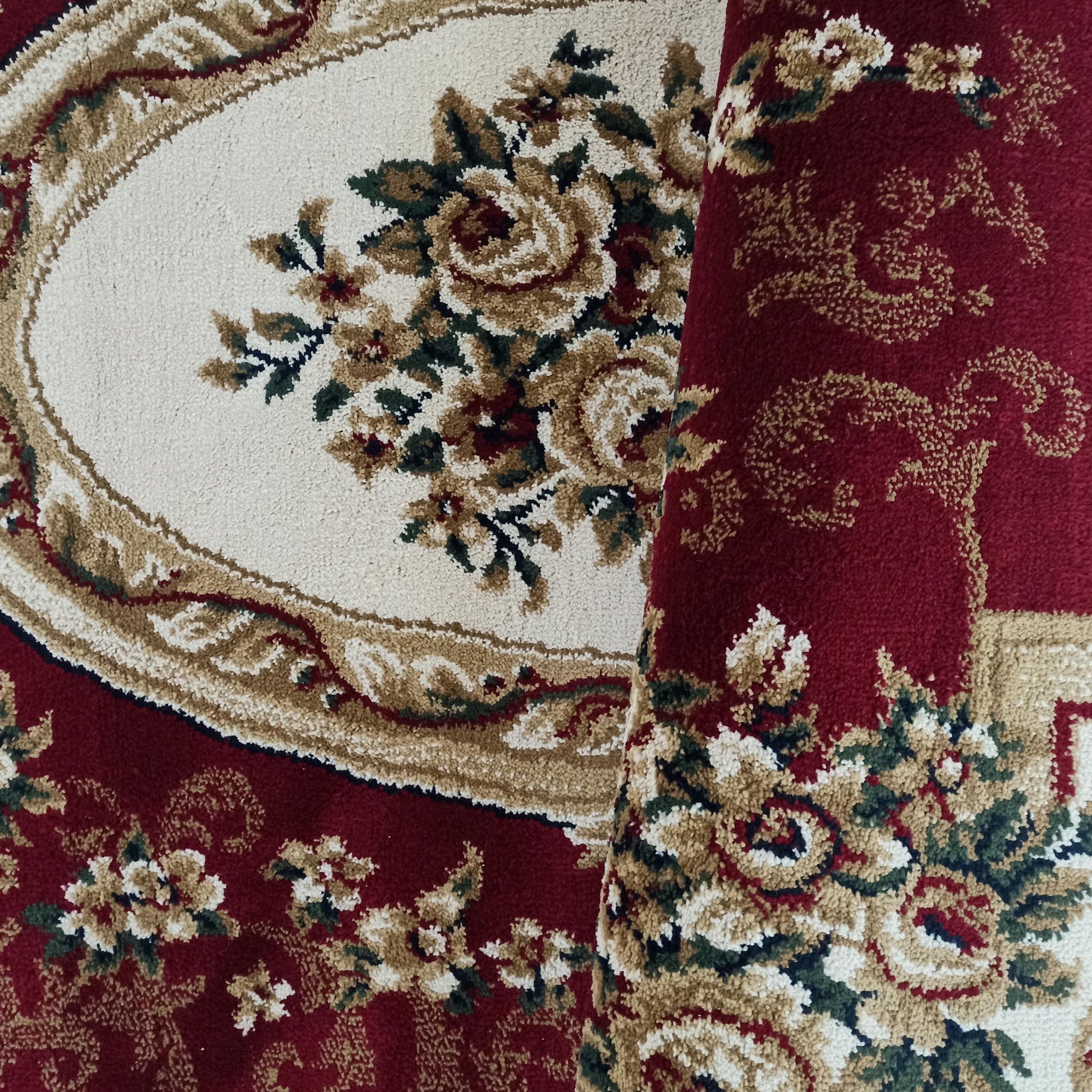 Tapis bordeaux à motifs floraux et ornementaux. Un médaillon central crème est orné de roses beiges, rouges et de feuillages verts