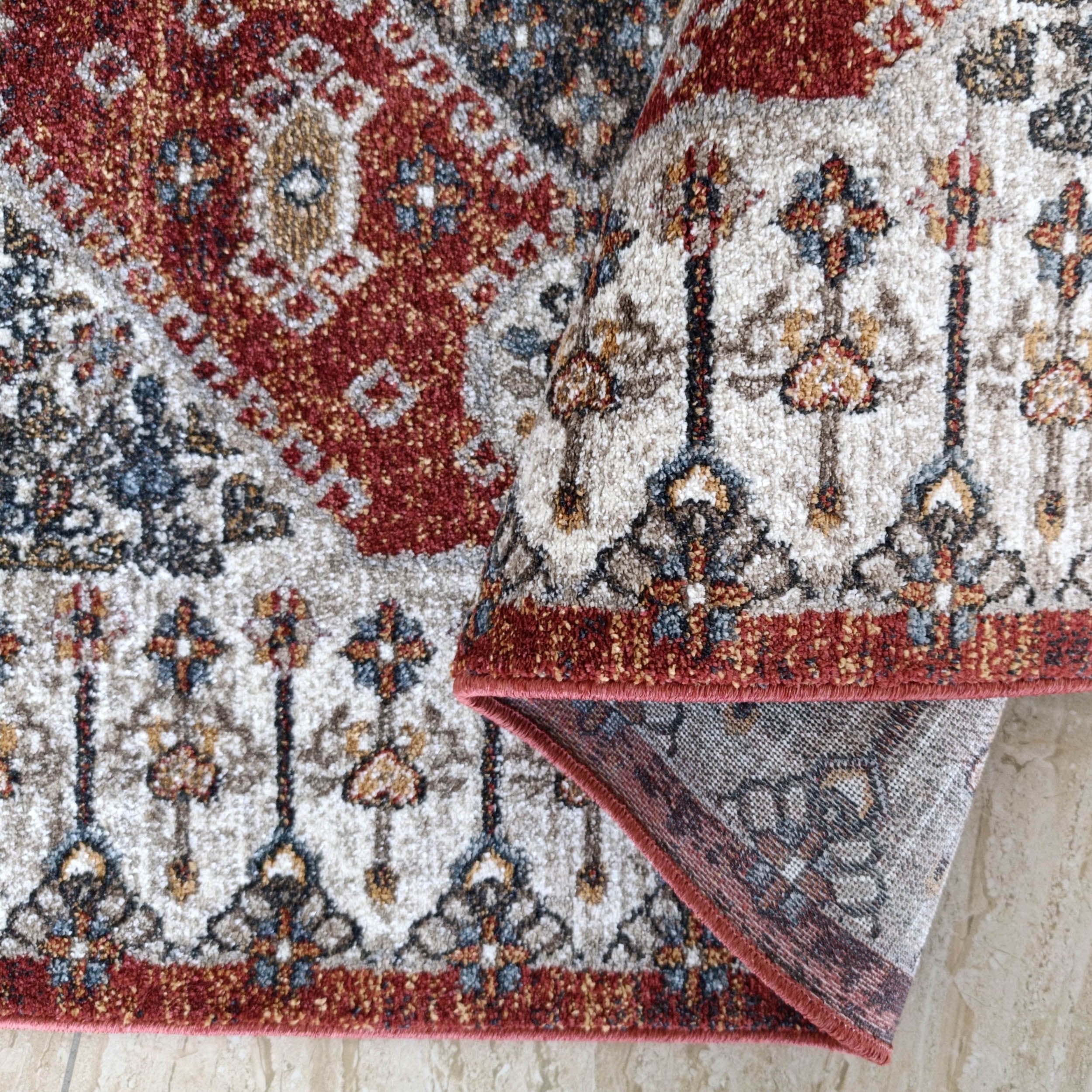 Tapis texturé aux motifs élaborés rouge bordeaux, crème, bleu et ocre, plié sur un carrelage beige clair