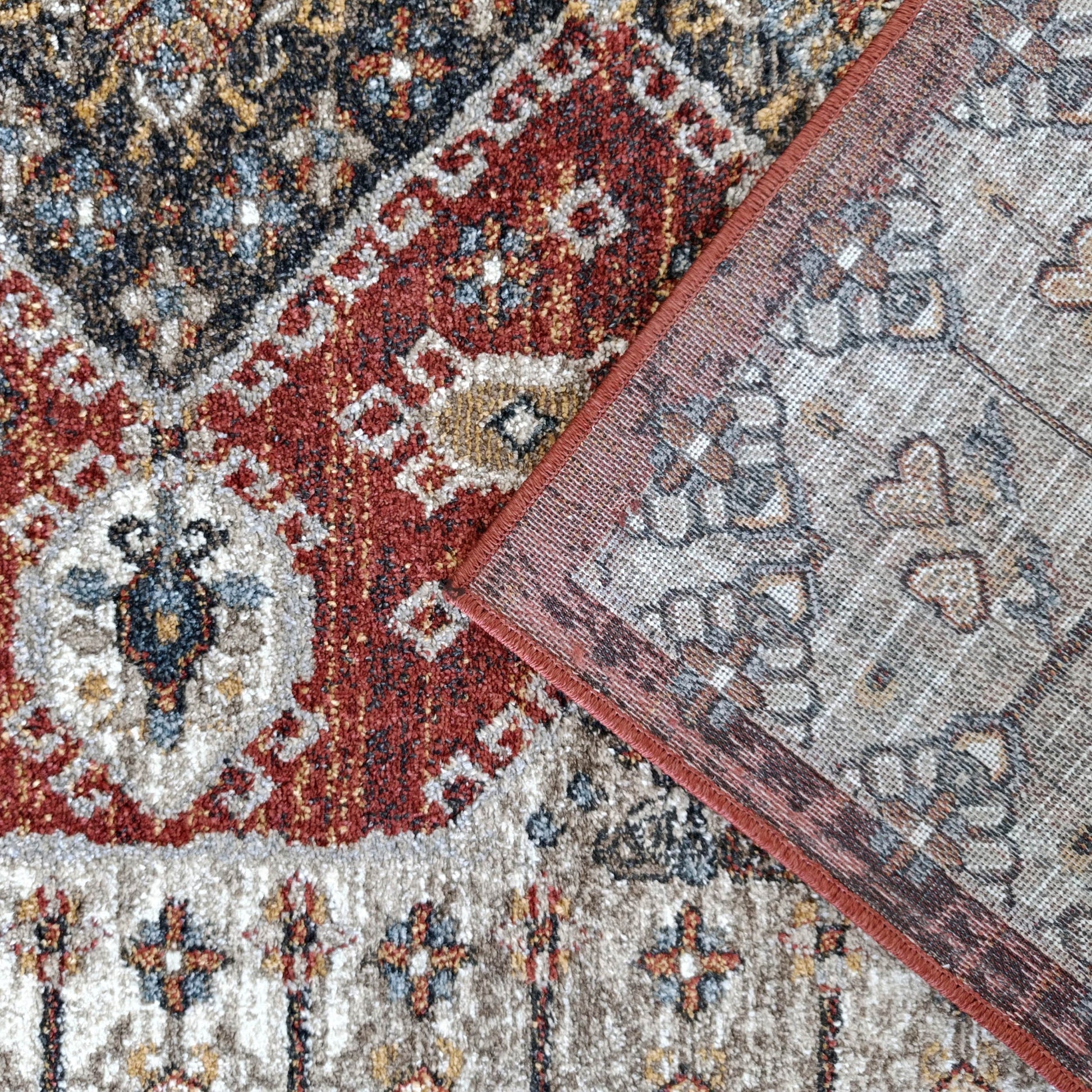 Tapis oriental bordeaux, noir, beige, bleu, un coin replié révèle l'envers gris tissé à bordure rouge