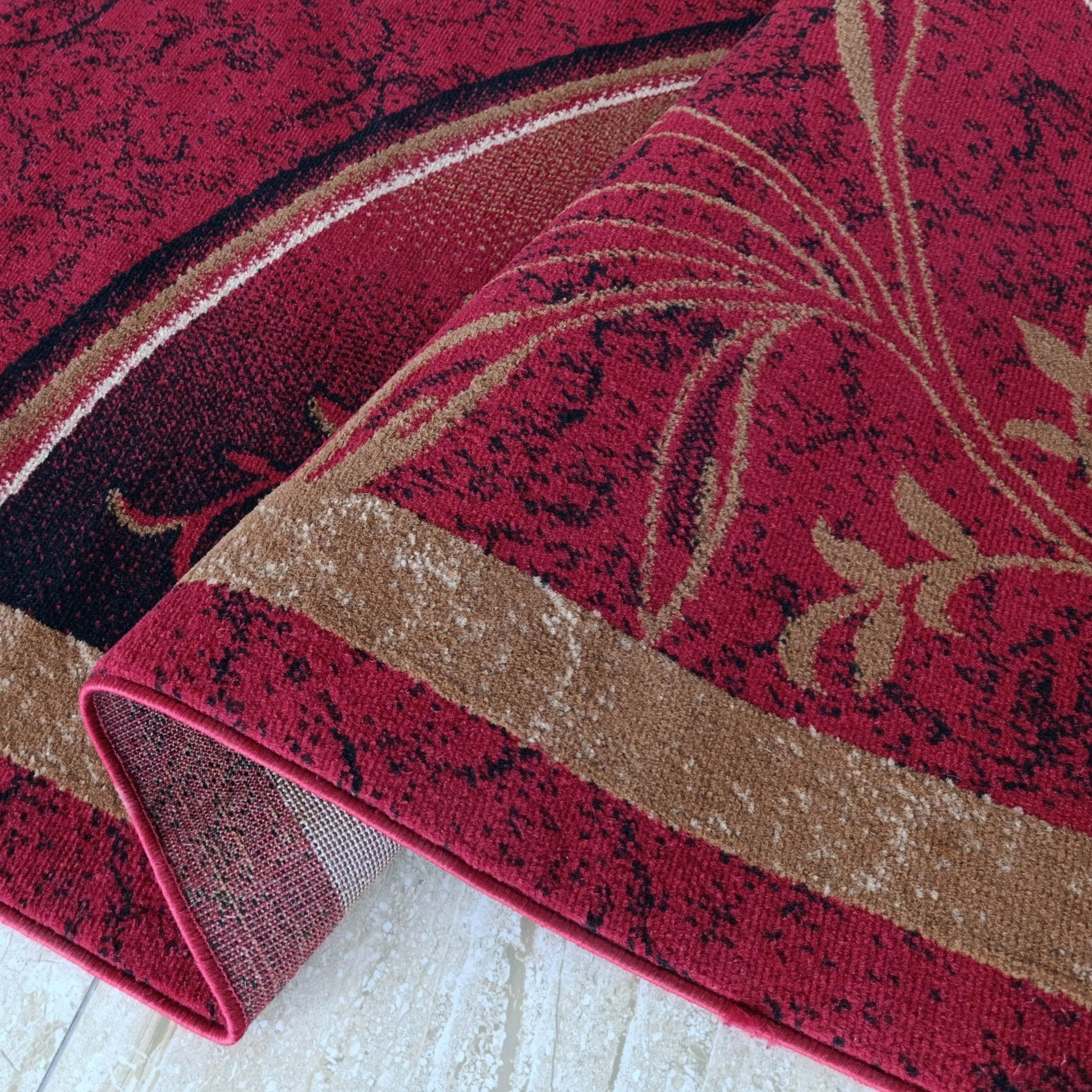 Tapis rouge bordeaux avec motifs floraux beiges et taches noires, partiellement roulé sur un sol clair