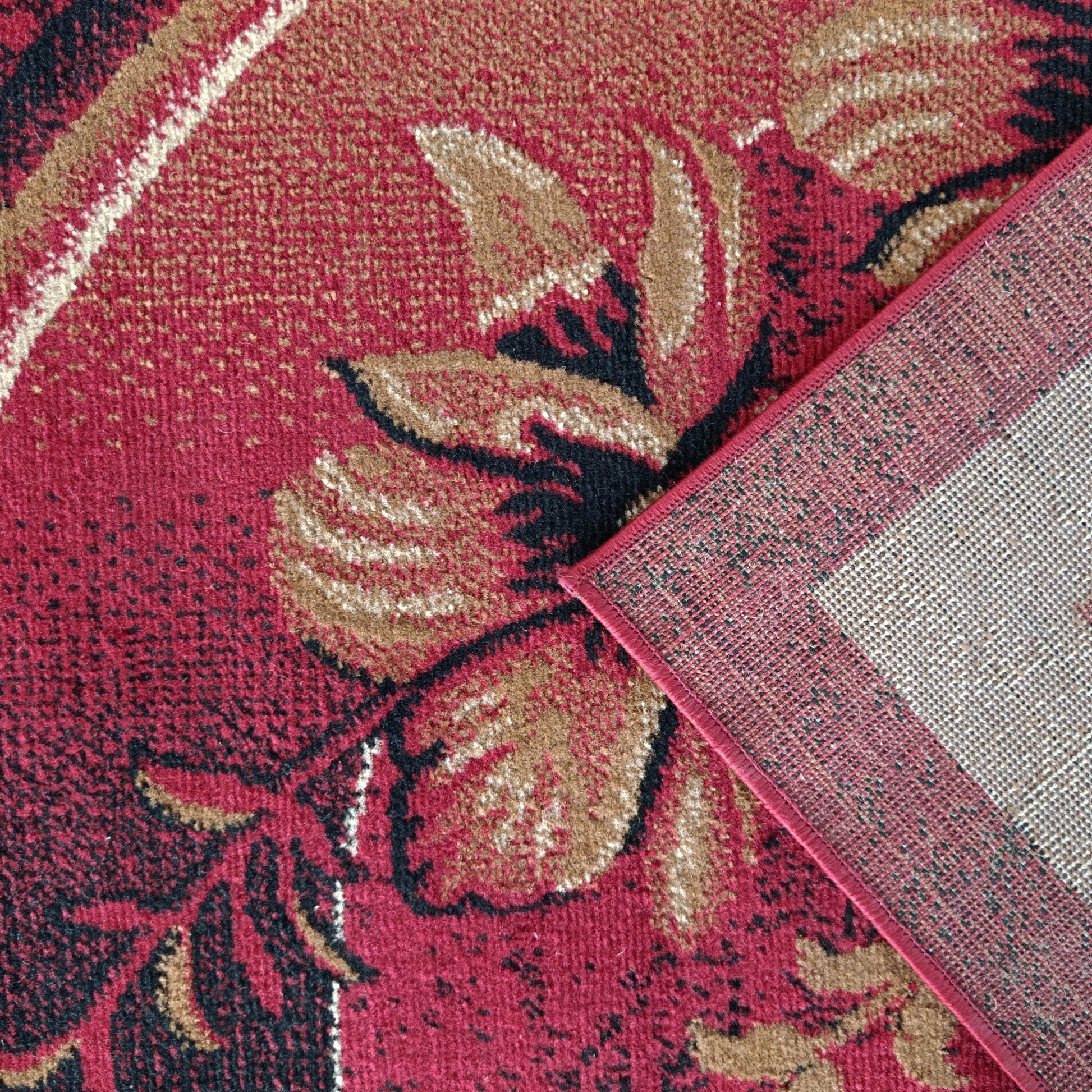 Tapis bordeaux à motifs floraux beiges et noirs, un coin soulevé révélant son dos tissé gris et liseré rouge