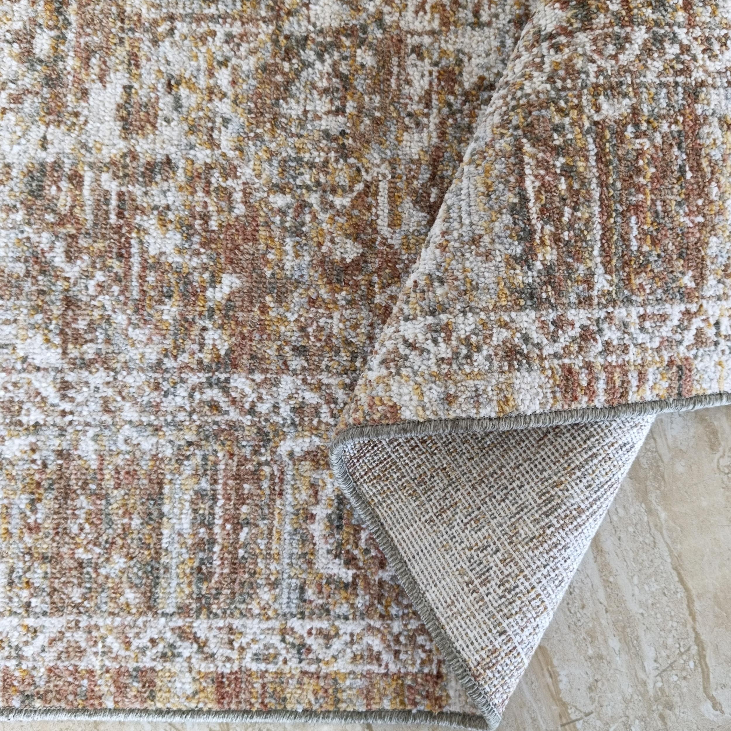 Un tapis texturé aux couleurs mélangées crème, marron, jaune et gris, avec son revers tissé visible sur un sol carrelé clair