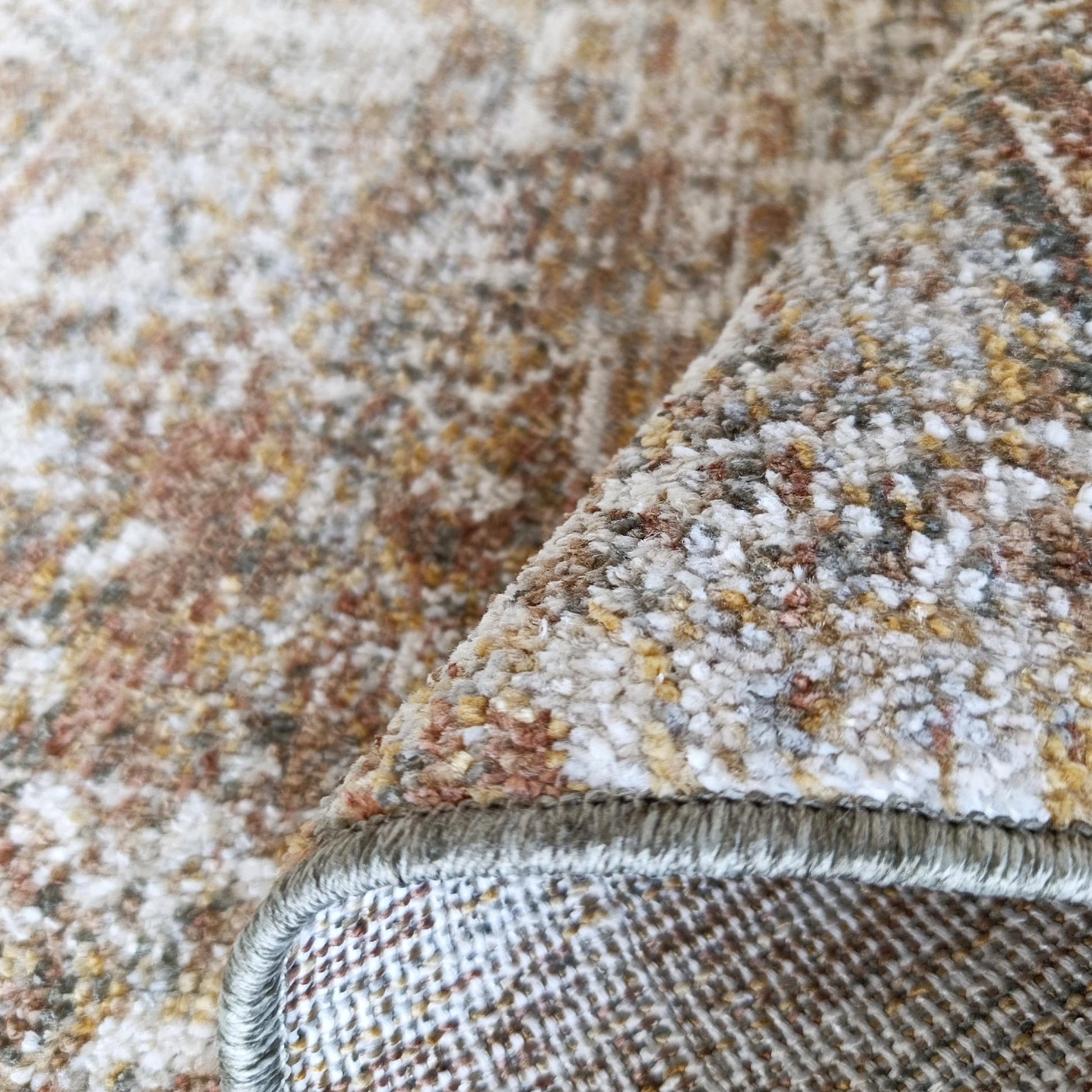 Tapis moelleux aux motifs tachetés beige, marron, blanc, doré et gris, avec un coin relevé et une bordure cousue