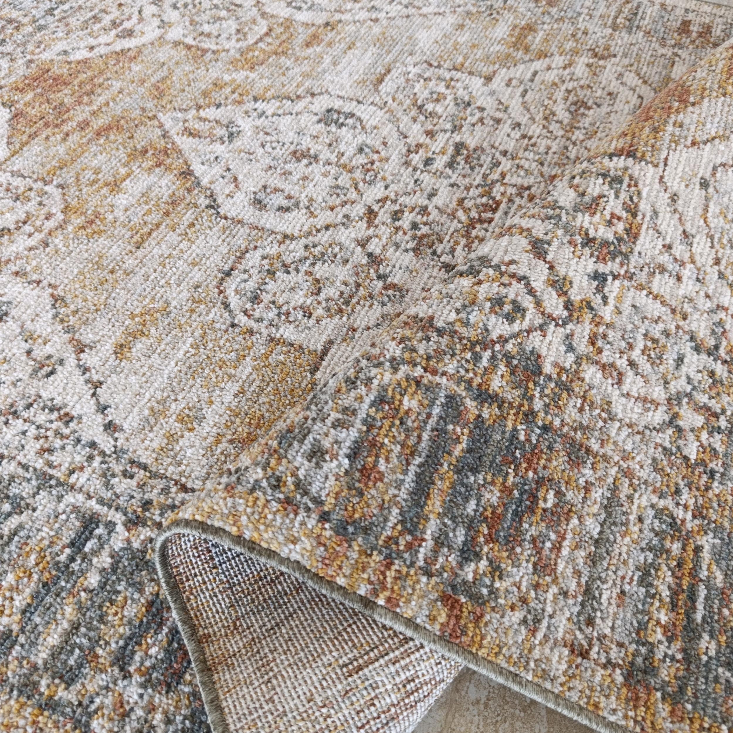 Un tapis moelleux partiellement enroulé, aux motifs ornementaux crème, ocre, rouille et gris-bleu