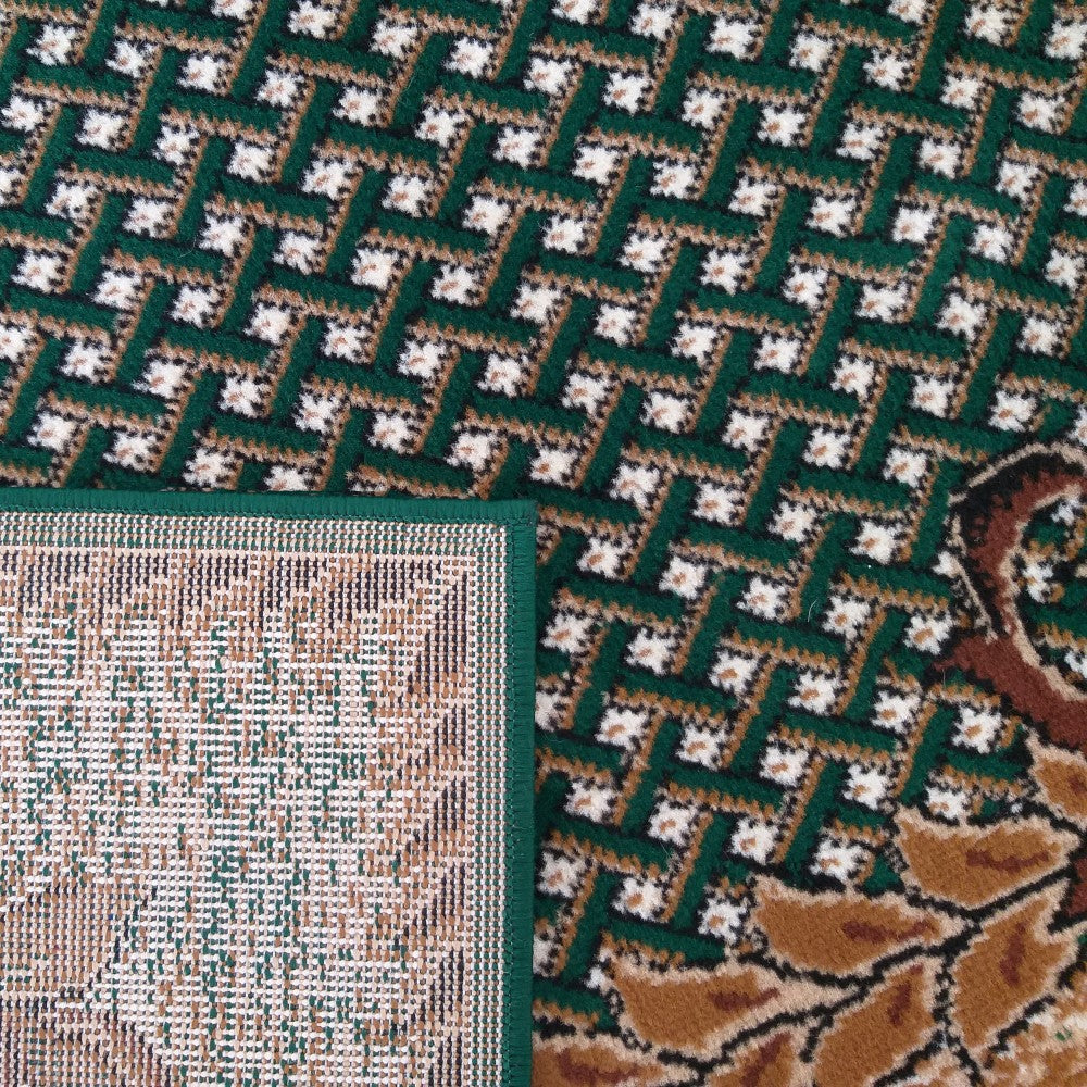 Tapis vert foncé à motifs géométriques blancs et bruns en zigzag, avec une section florale marron et le revers tissé visible sur un coin