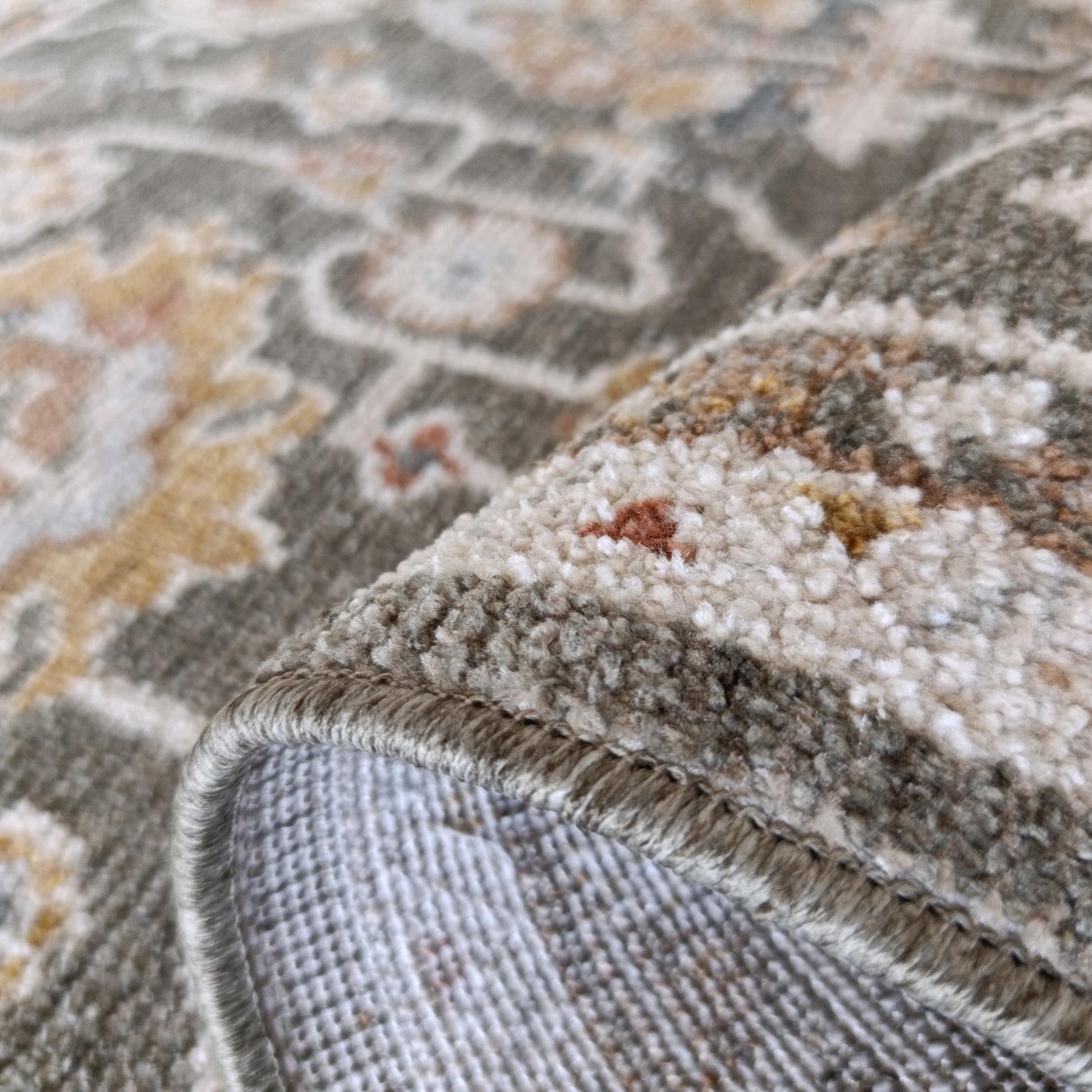 Un tapis roulé aux motifs ornementaux vert sauge, beige clair et jaune. La texture douce et l'envers tissé sont visibles