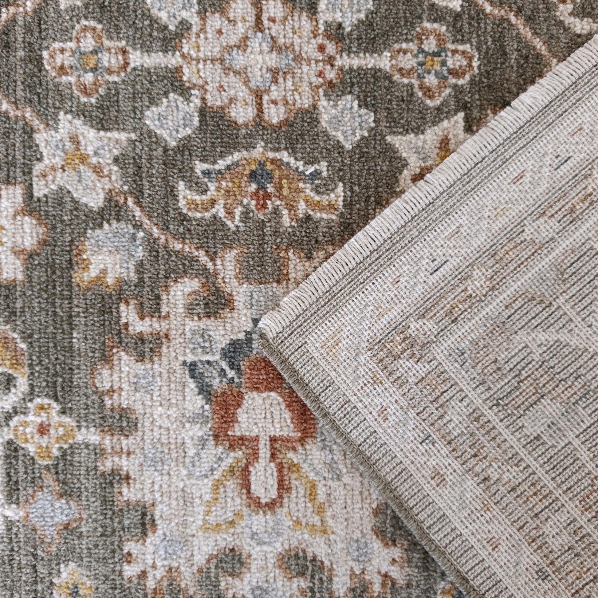 Tapis à poils doux aux motifs ornementaux vert-gris, crème, ocre et bleu, avec un revers tissé beige et des franges