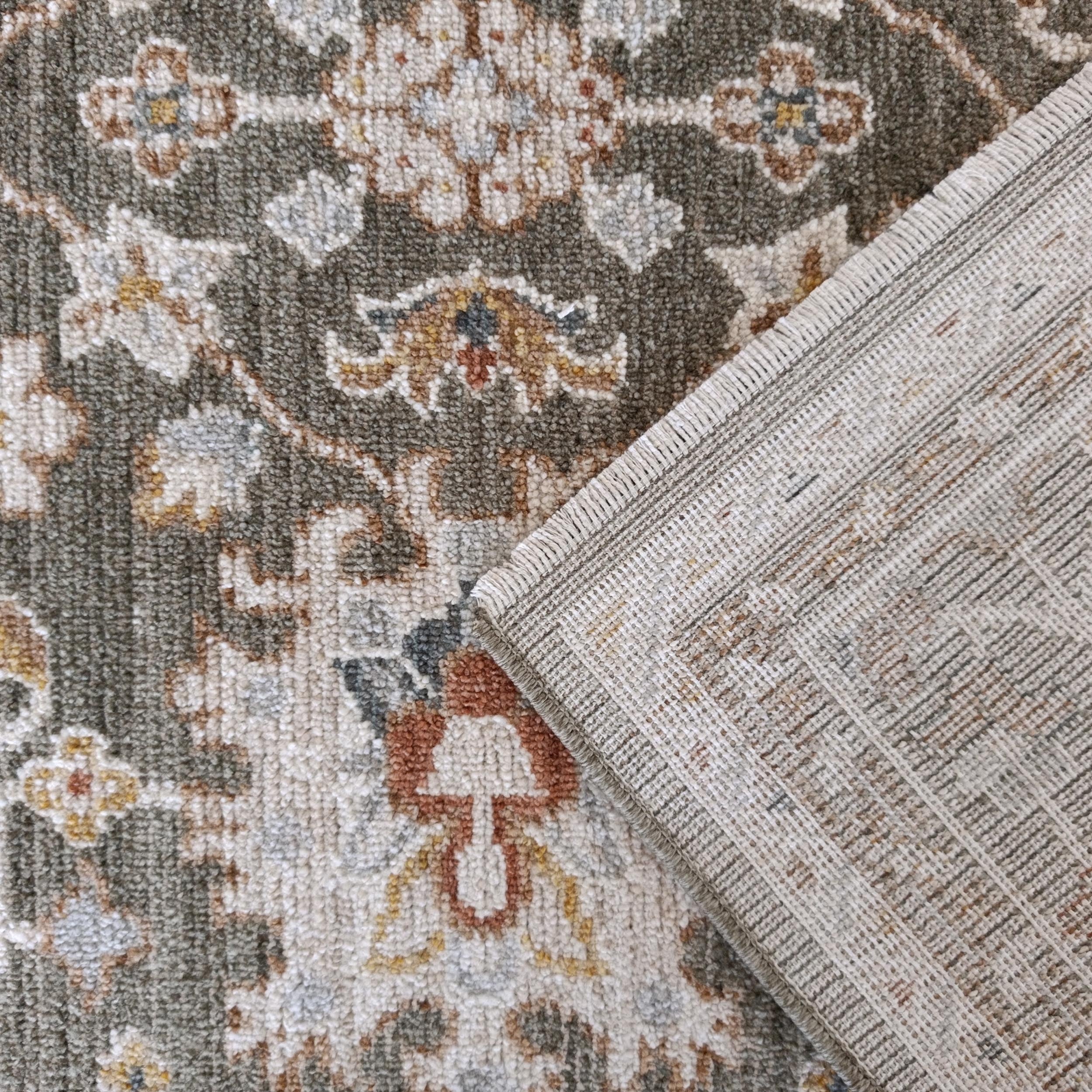 Tapis à poils doux aux motifs ornementaux vert-gris, crème, ocre et bleu, avec un revers tissé beige et des franges