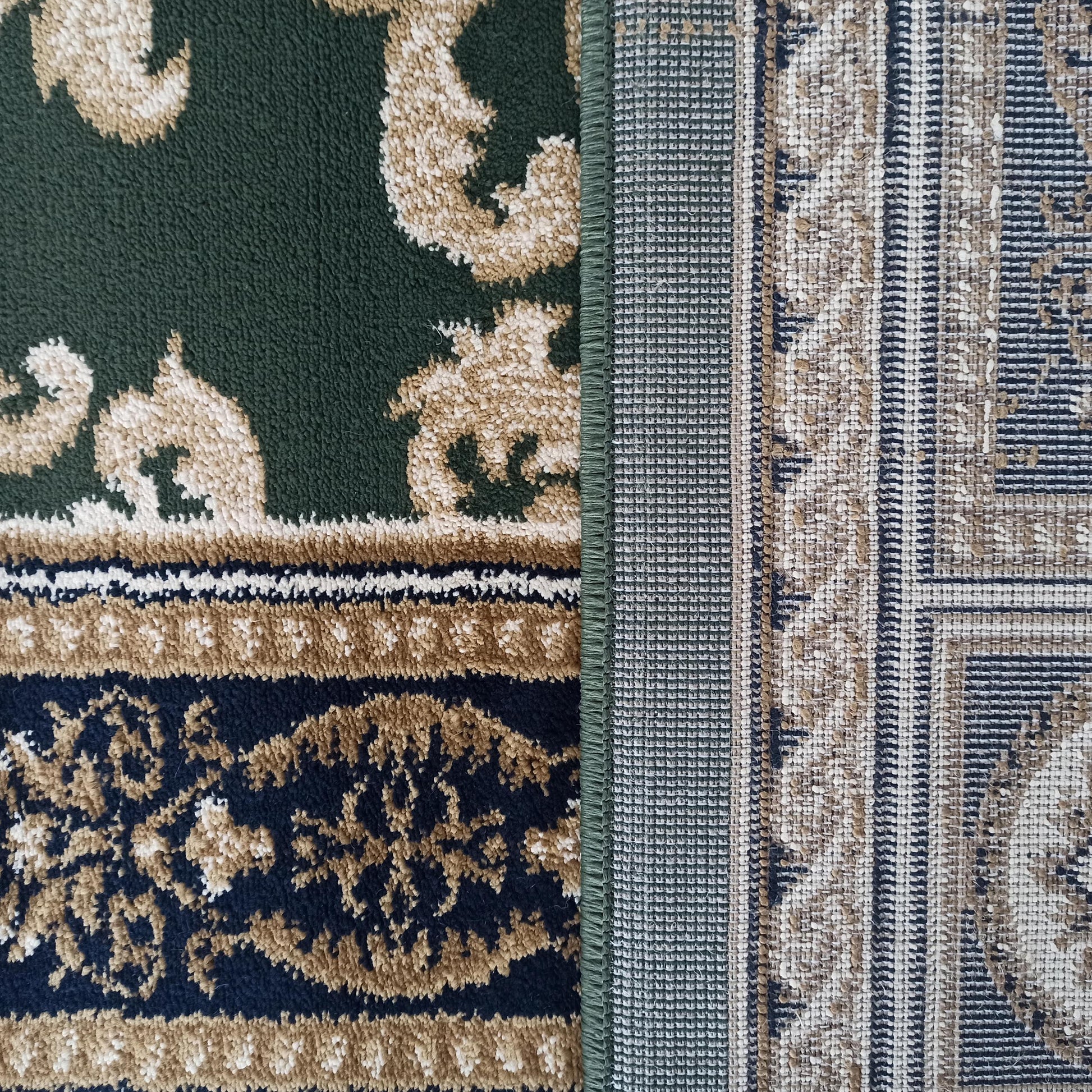 Un tapis vert foncé, beige et bleu marine avec des motifs ornementaux, montrant également son envers tissé géométrique
