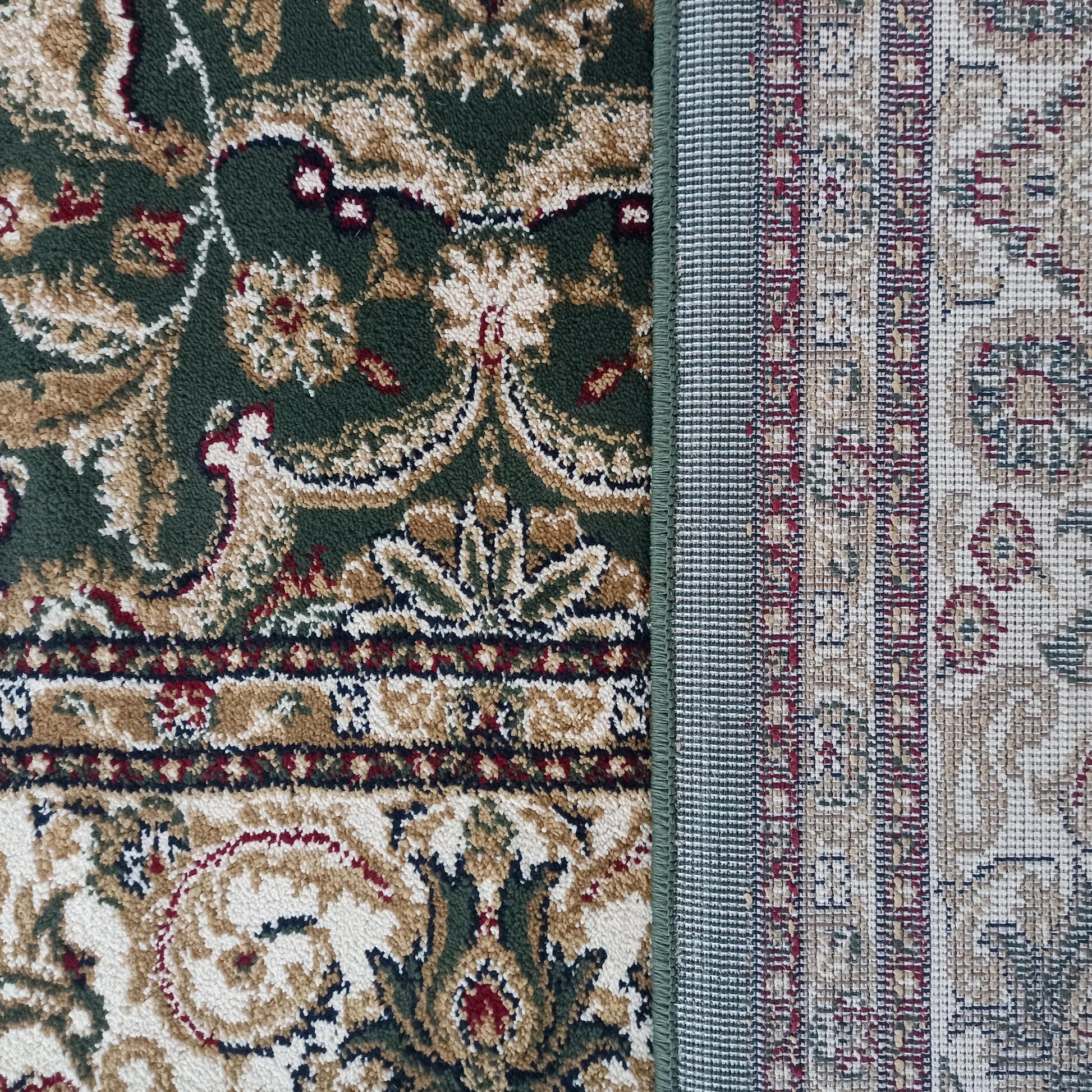 Gros plan sur un tapis au motif floral vert foncé, beige, crème et bordeaux, montrant son envers tissé et son bord ourlé