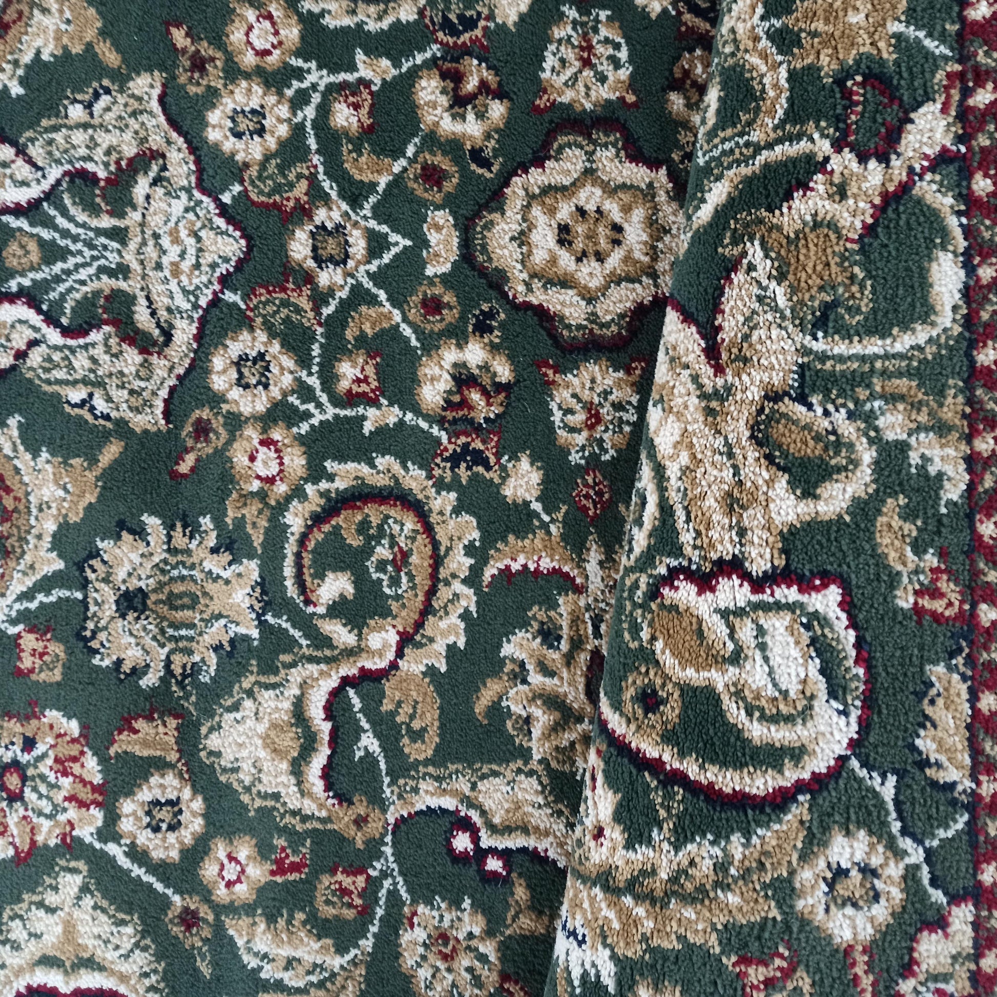 Tapis vert foncé aux motifs floraux et arabesques en beige, crème et bordeaux, avec une texture bouclée