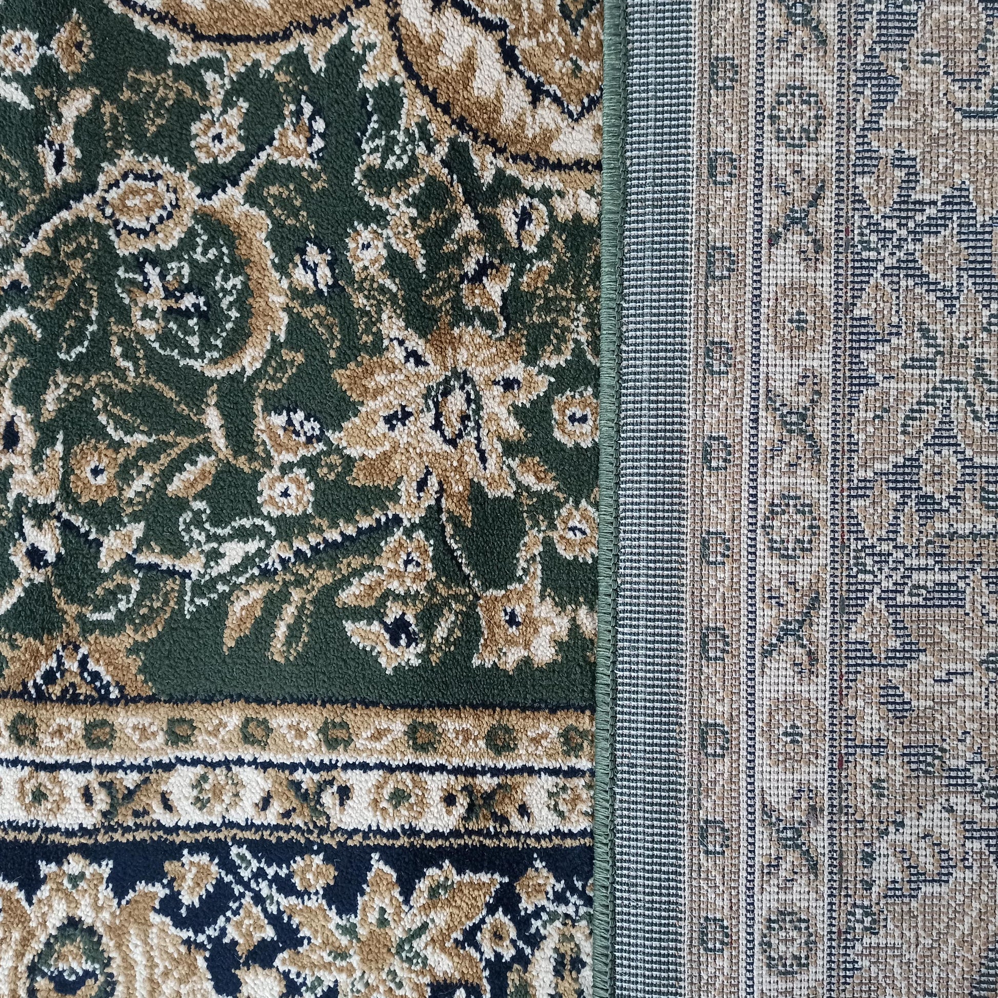 Tapis avec motifs ornementaux beiges, noirs et crème sur fond vert foncé, l'envers tissé beige et gris apparaît à droite