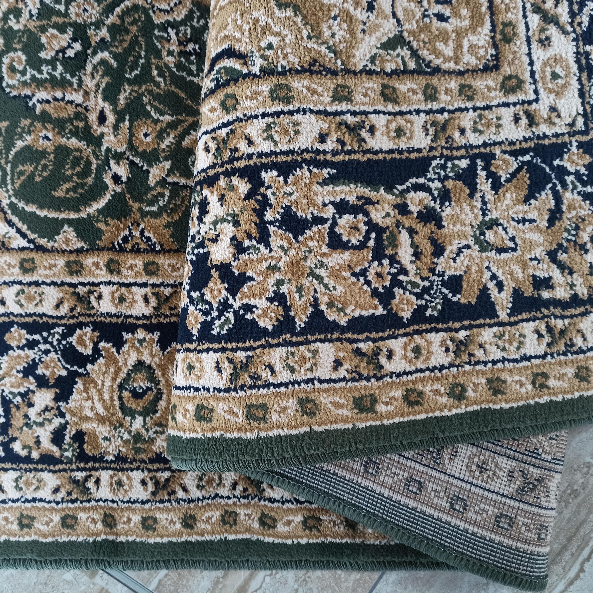Tapis plissé aux motifs floraux détaillés verts forêt, beiges, bleus nuit et crème, posé sur un carrelage