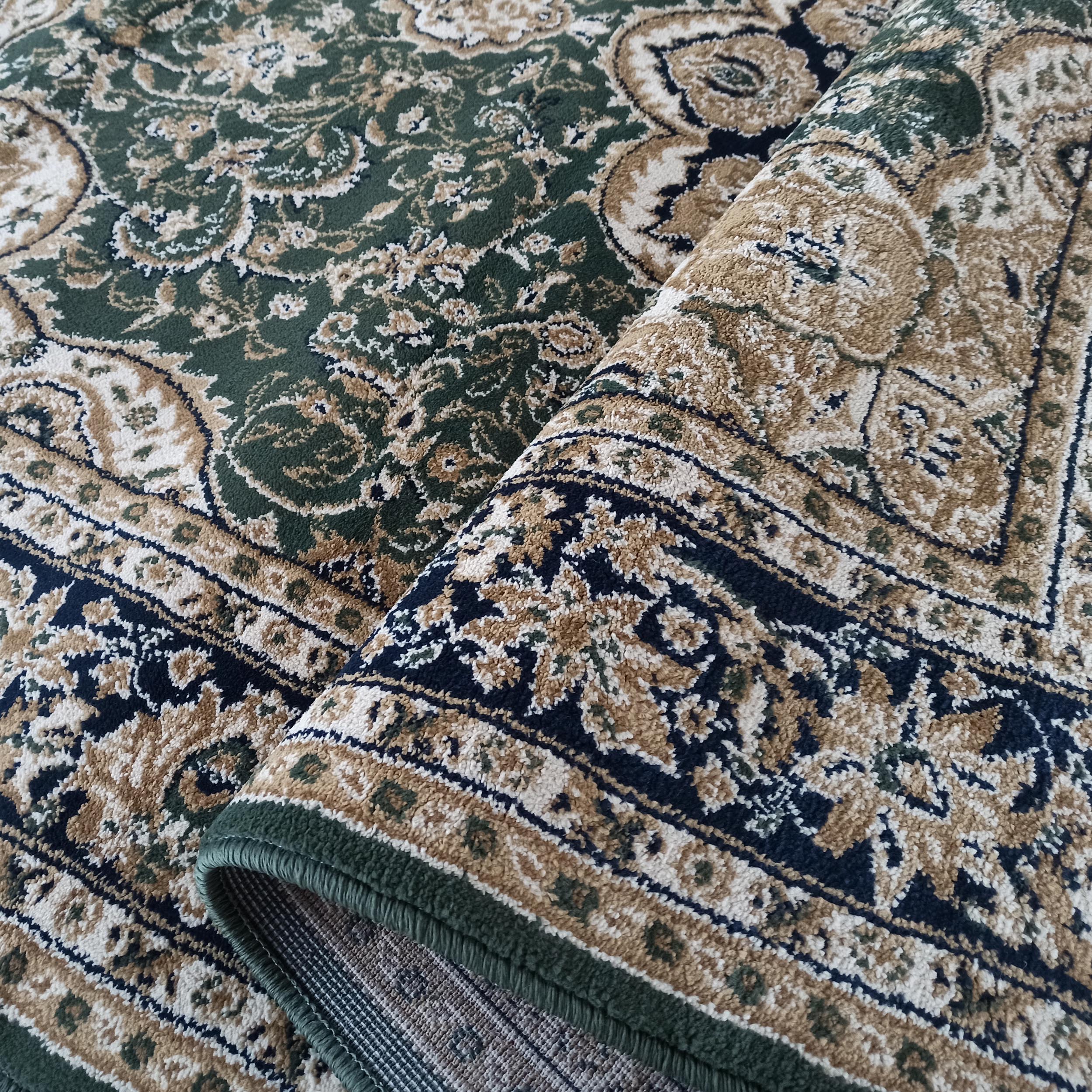 Tapis partiellement roulé avec des motifs orientaux complexes vert foncé, beige, crème et bleu marine, révélant son envers tissé