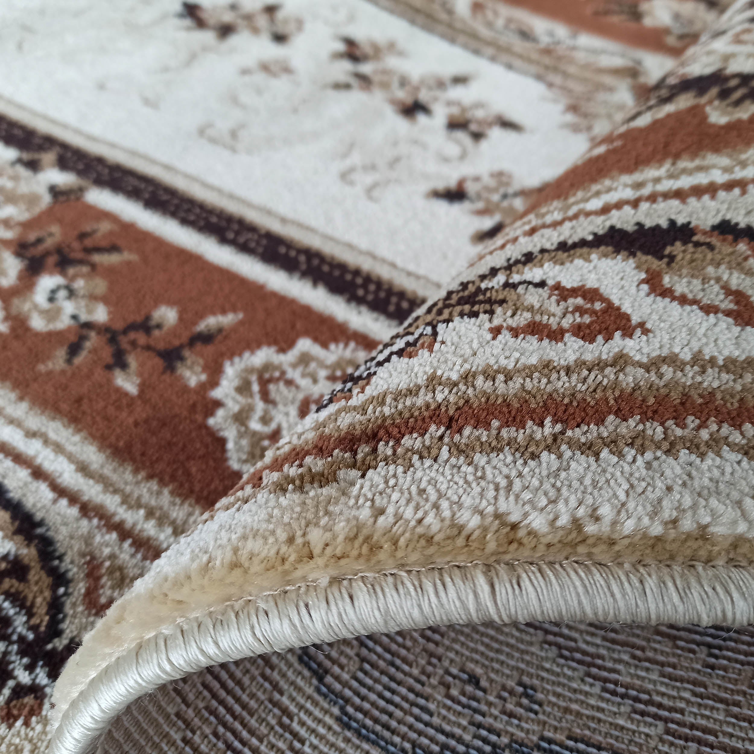 Gros plan sur un tapis moelleux partiellement roulé, avec des motifs floraux et rayures beiges, crème et marron