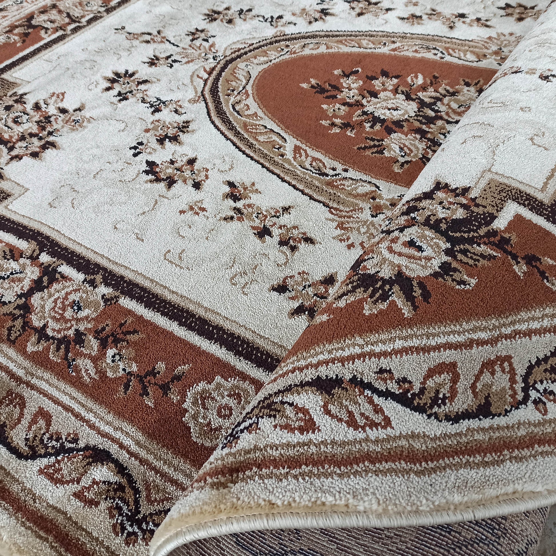 Tapis à motifs classiques floraux beiges, marron clair et foncé, partiellement roulé, au toucher moelleux