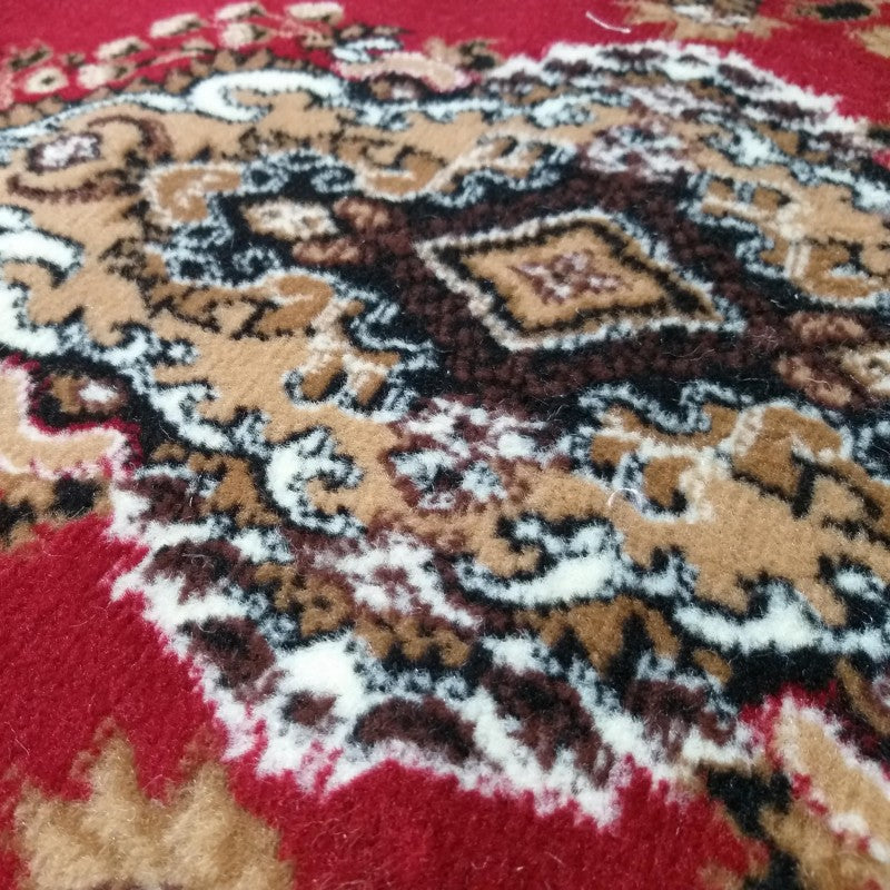 Tapis rouge avec des motifs ornementaux beige, marron foncé et blanc, en gros plan sur la texture textile