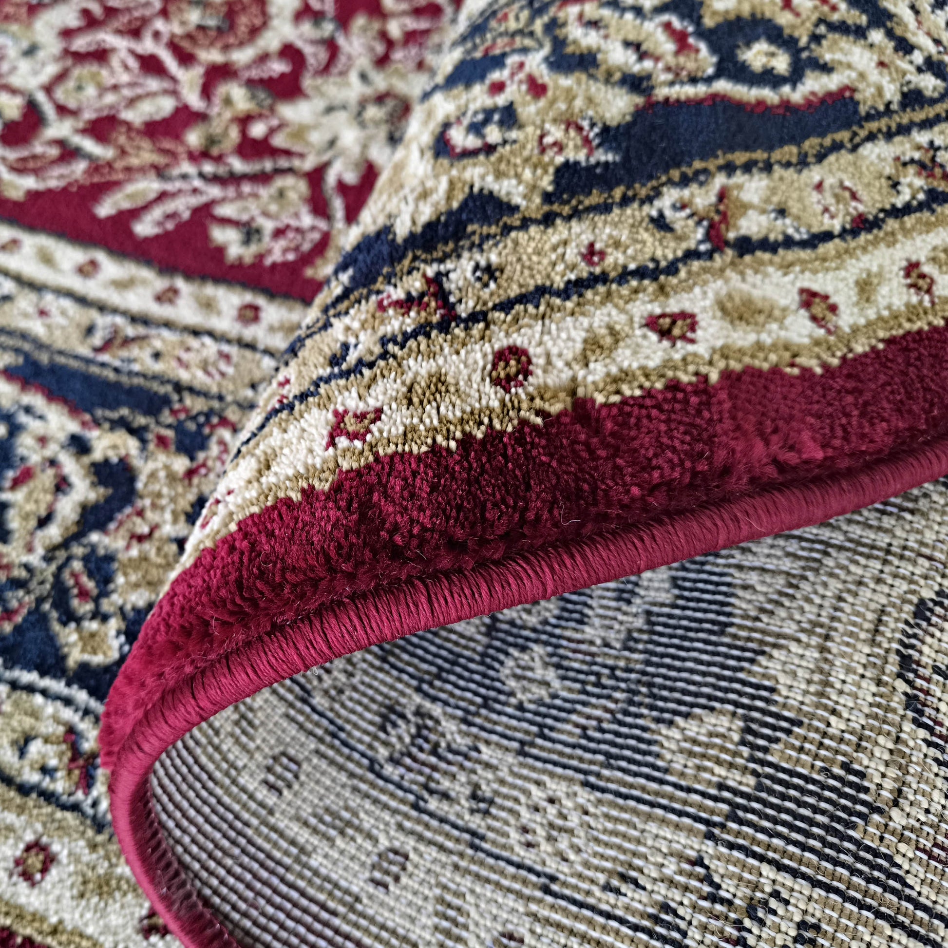 Gros plan sur un tapis moelleux aux motifs floraux traditionnels rouges, bleus, beiges et crème, roulé pour montrer son dos tissé
