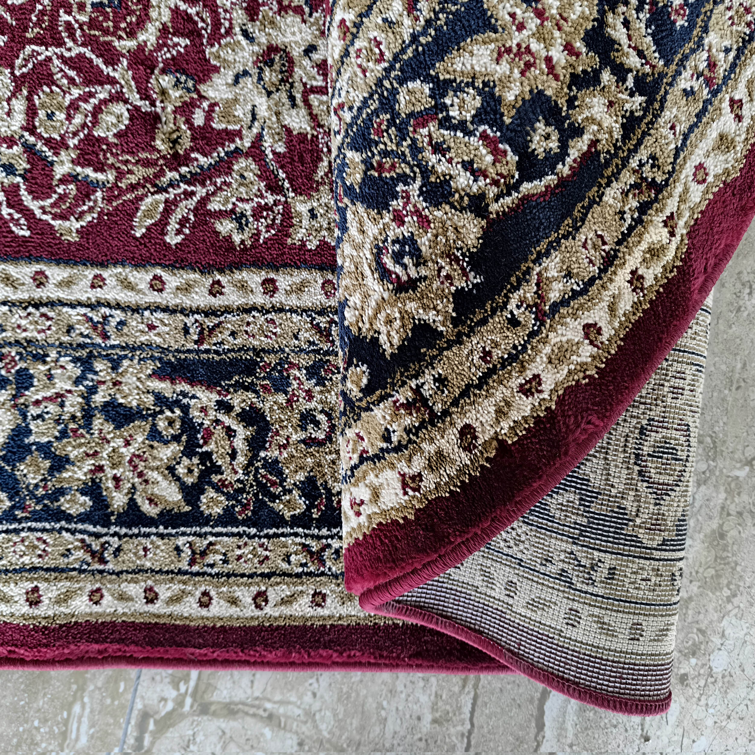 Tapis à motifs floraux et arabesques bordeaux, bleu marine, beige et blanc cassé, partiellement enroulé
