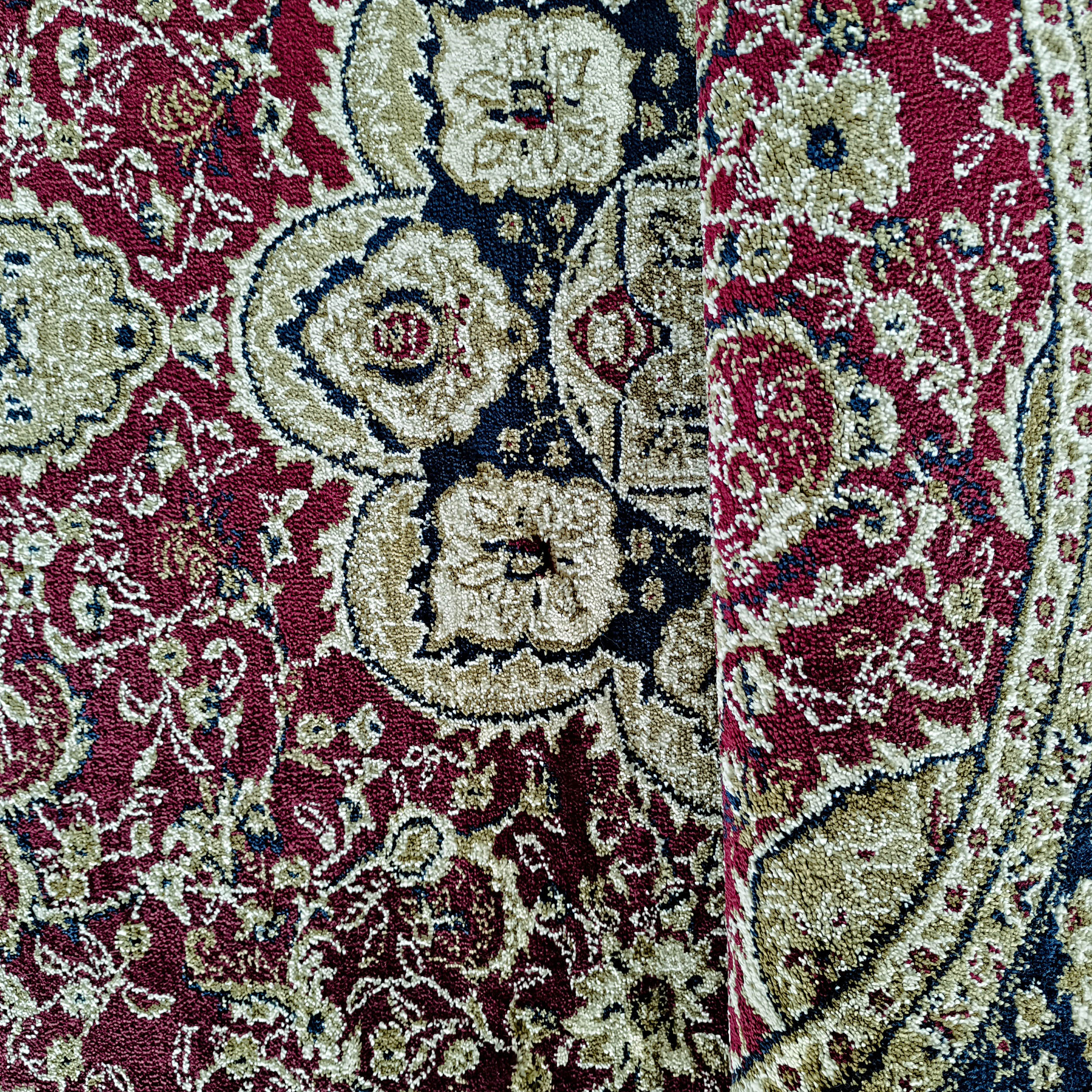 Tapis aux motifs traditionnels fleuris en bordeaux, beige, bleu marine et kaki, avec un pli visible sur la droite