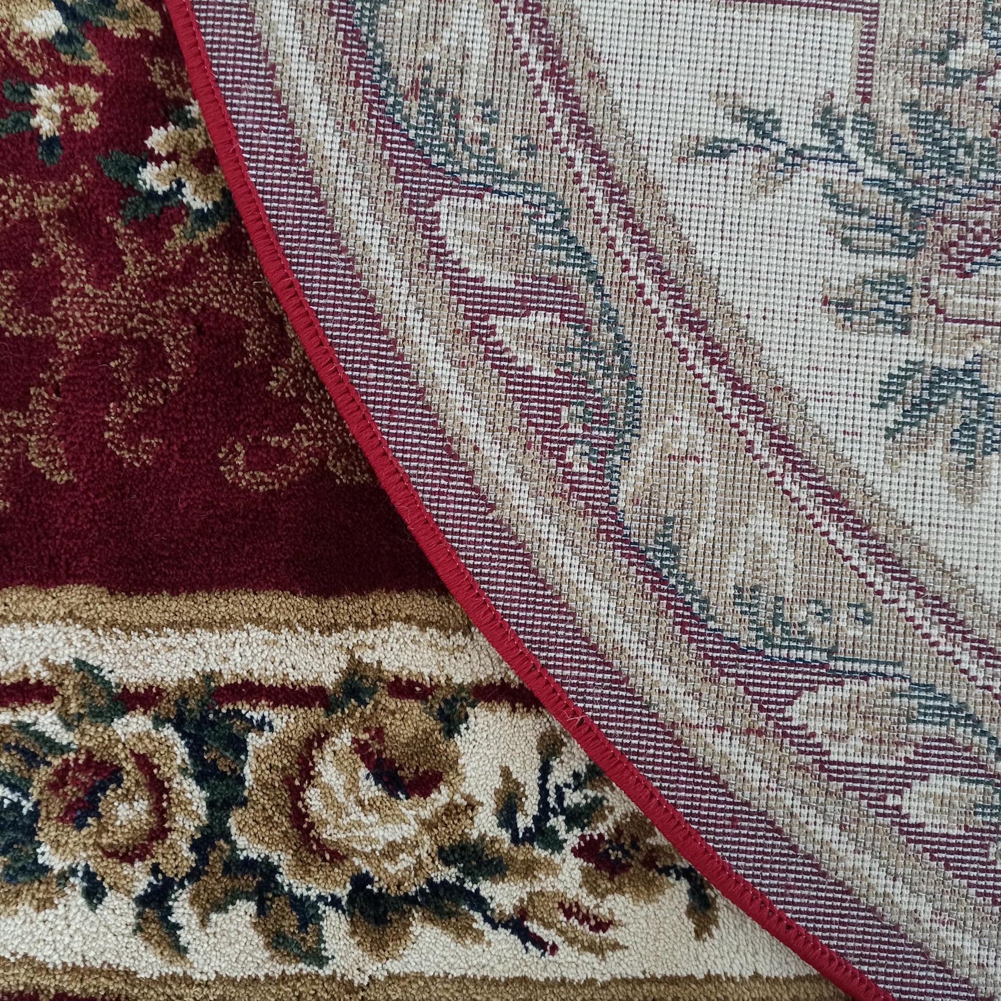 Tapis floral rouge, crème et vert, une partie retournée montrant son envers tissé beige à motifs et sa bordure rouge