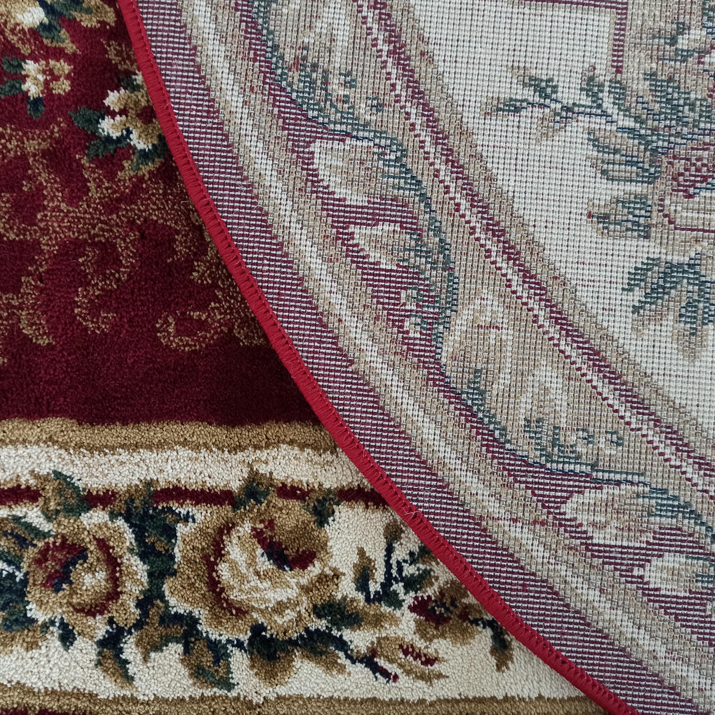 Tapis floral rouge, crème et vert, une partie retournée montrant son envers tissé beige à motifs et sa bordure rouge