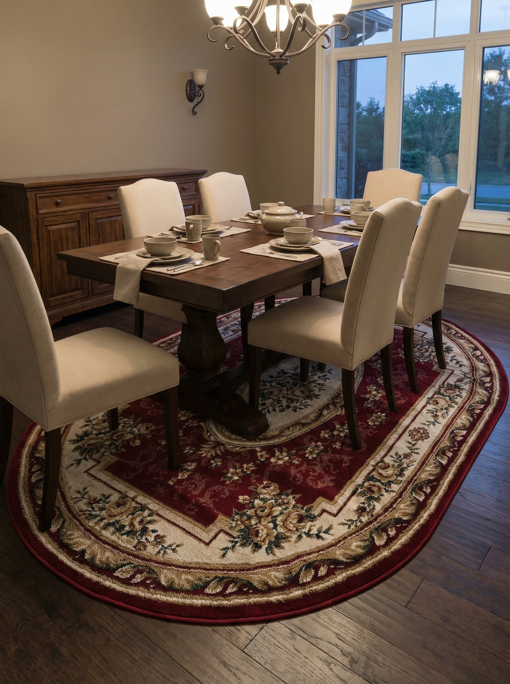 Tapis ovale rouge bordeaux orné de motifs floraux classiques crème et dorés, avec une large bordure claire, au sol d'une salle à manger