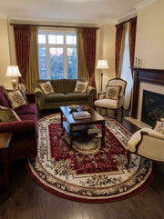 Tapis ovale bordeaux à motifs floraux crème et verts avec bordure beige, posé sur un parquet foncé dans un salon élégant